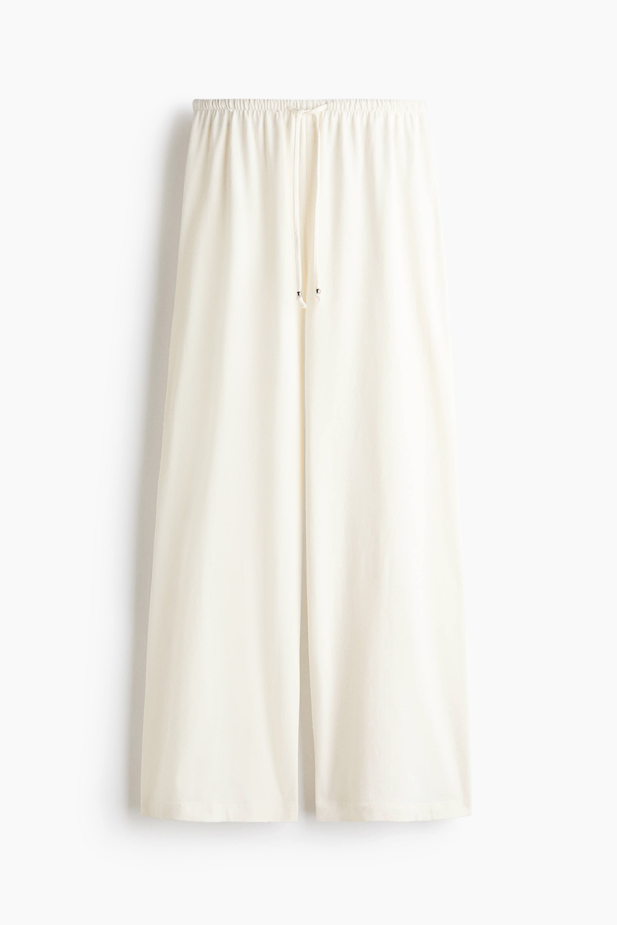 View larger image: Loose-fit trousers are showcased from the front, crafted in soft off-white cotton jersey, featuring an elasticated, drawstring waist with visible metal-tipped drawstrings and wide legs.