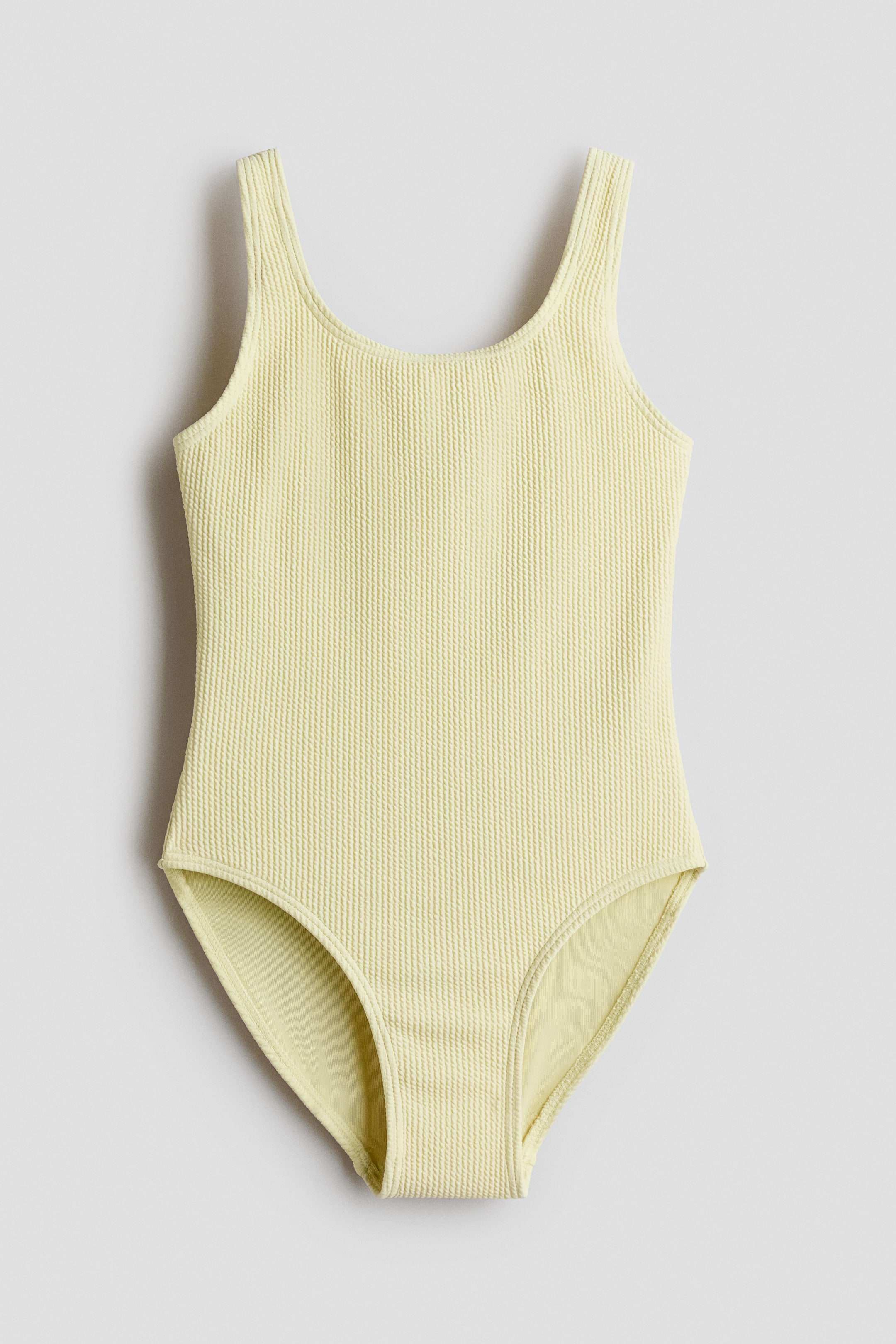 Se større billede: En lysegul ribbet badedragt vises forfra, med en rund halsudskæring, brede skulderstropper og en lysere gul foring synlig ved benåbningerne.