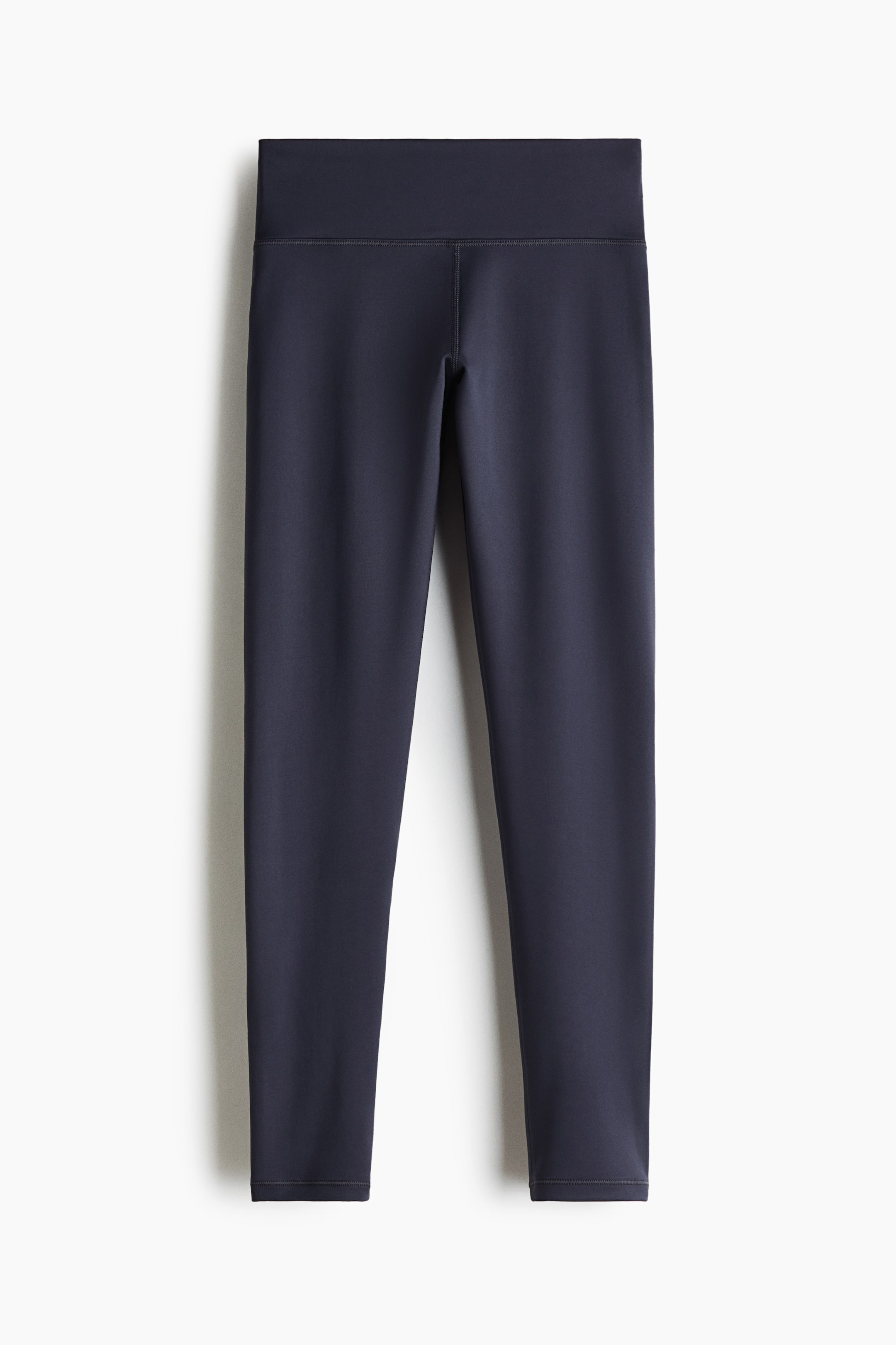 View larger image: Sports leggings are showcased from a front perspective, featuring a dark blue colour and a wide, high-rise waistband. Flatlock seams detail the inner legs, and the design is form-fitting, extending to the ankles.