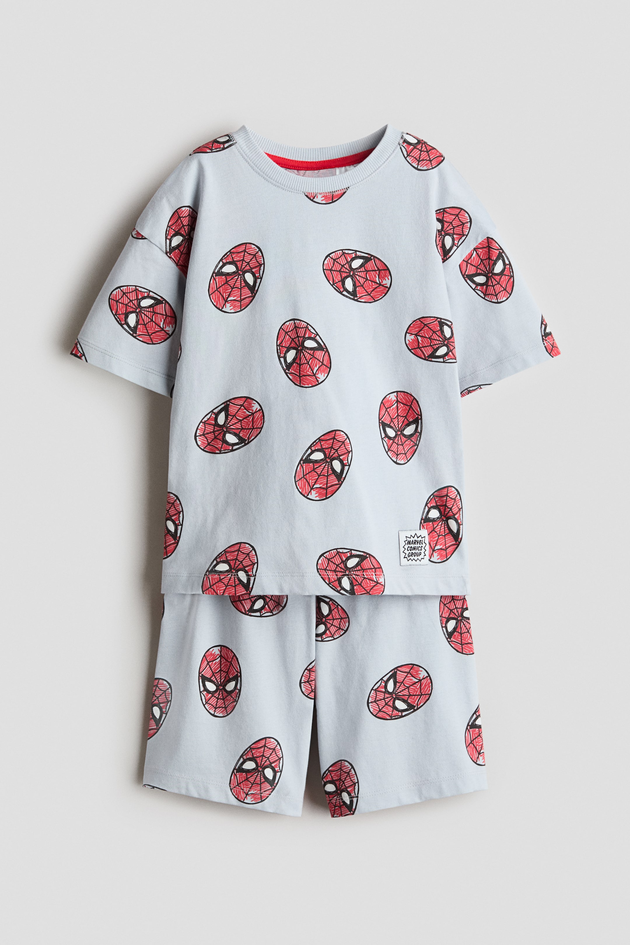 Ver imagem maior: Um conjunto de pijama composto por uma T-shirt e calções a condizer, ambos feitos de jersey azul-claro suave, exibindo uma estampa completa de máscaras vermelhas do Homem-Aranha. A T-shirt é desenhada com um acabamento canelado em torno da gola e ombros descaídos, e os calções apresentam uma cintura elástica.