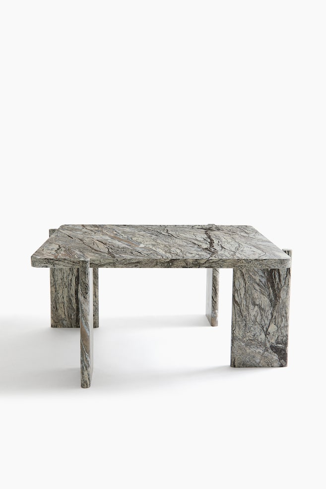 Une table basse rectangulaire en marbre gris et brun fortement veinÃ© est prÃ©sentÃ©e en vue Ã  trois quarts. Le design met en valeur un plateau Ã©pais aux angles arrondis, soutenu par quatre pieds en forme de dalles, positionnÃ©s perpendiculairement aux coins. - 1