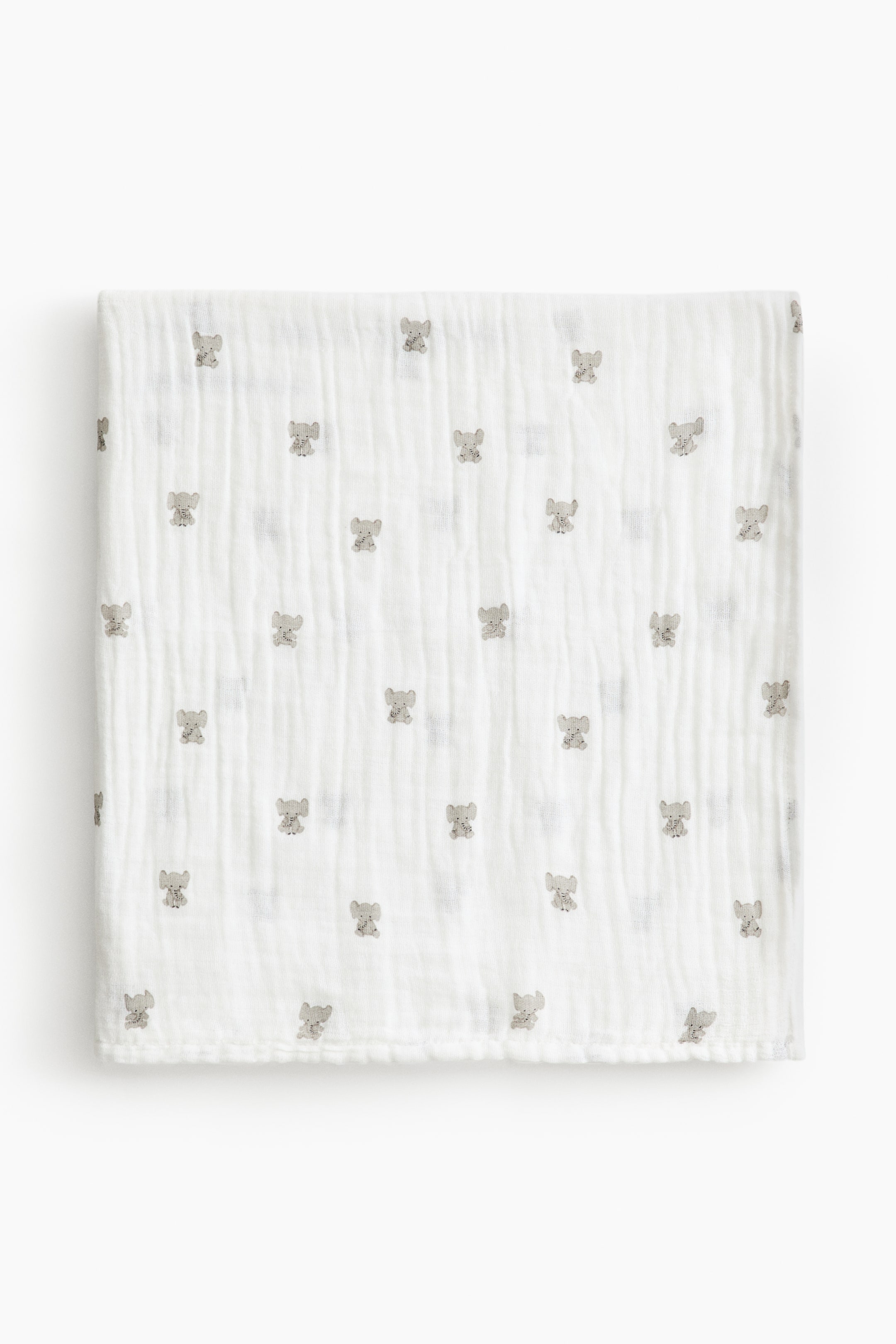 View larger image: A white baby blanket in a soft, crinkled muslin weave is shown folded flat from the front, displaying an all-over pattern of miniature gray elephant motifs.