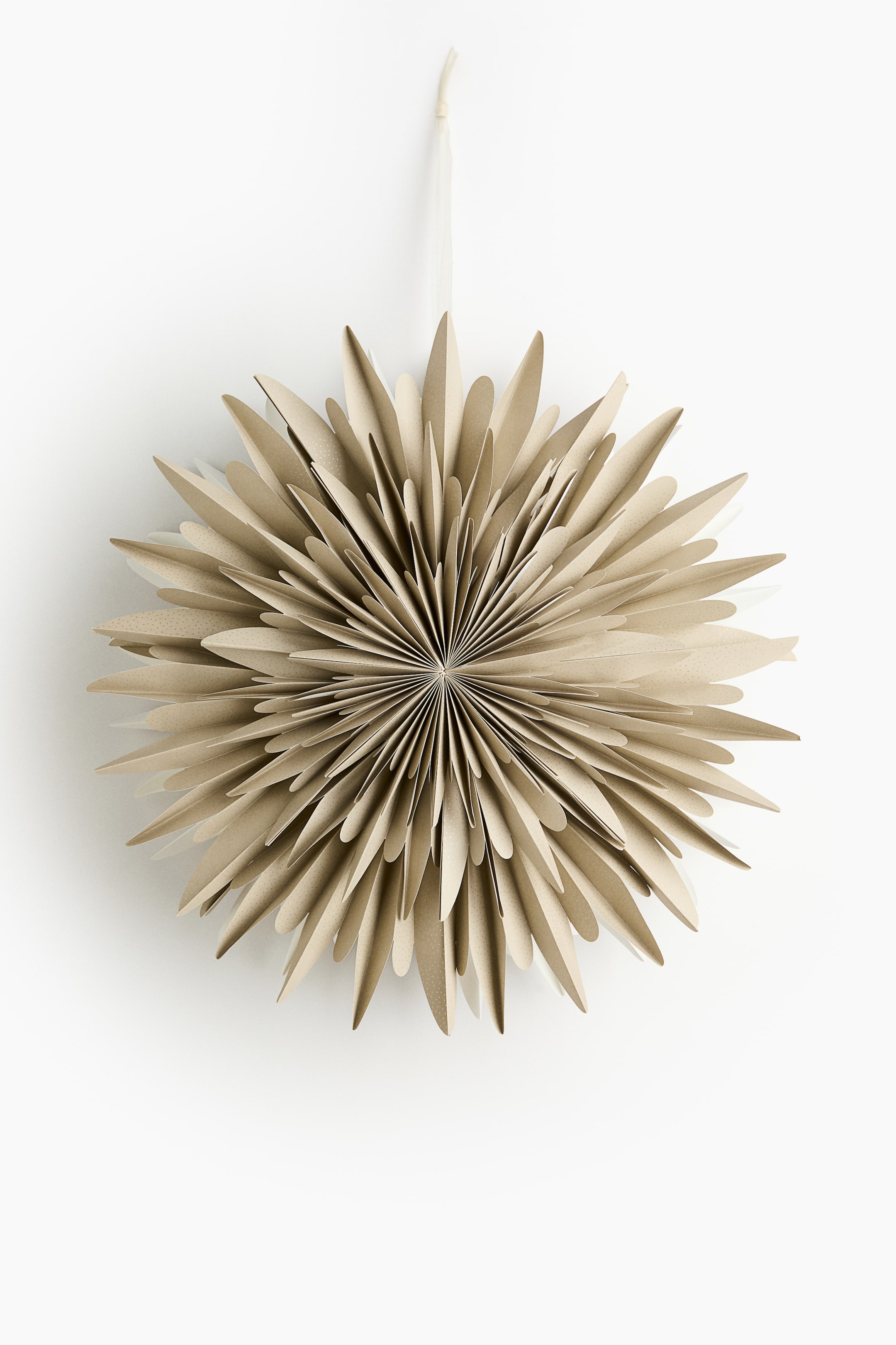 Se større billede: En papir stjerne præsenterer sin FRONT, der viser et design, der minder om en fjerlet snefnug. Den er konstrueret af flere lag af foldet, lysebrunt papir, hvor hvert stykke har blødt afrundede kanter og en subtil prikket tekstur, og et tyndt, lysefarvet bånd danner en løkke øverst til ophængning.