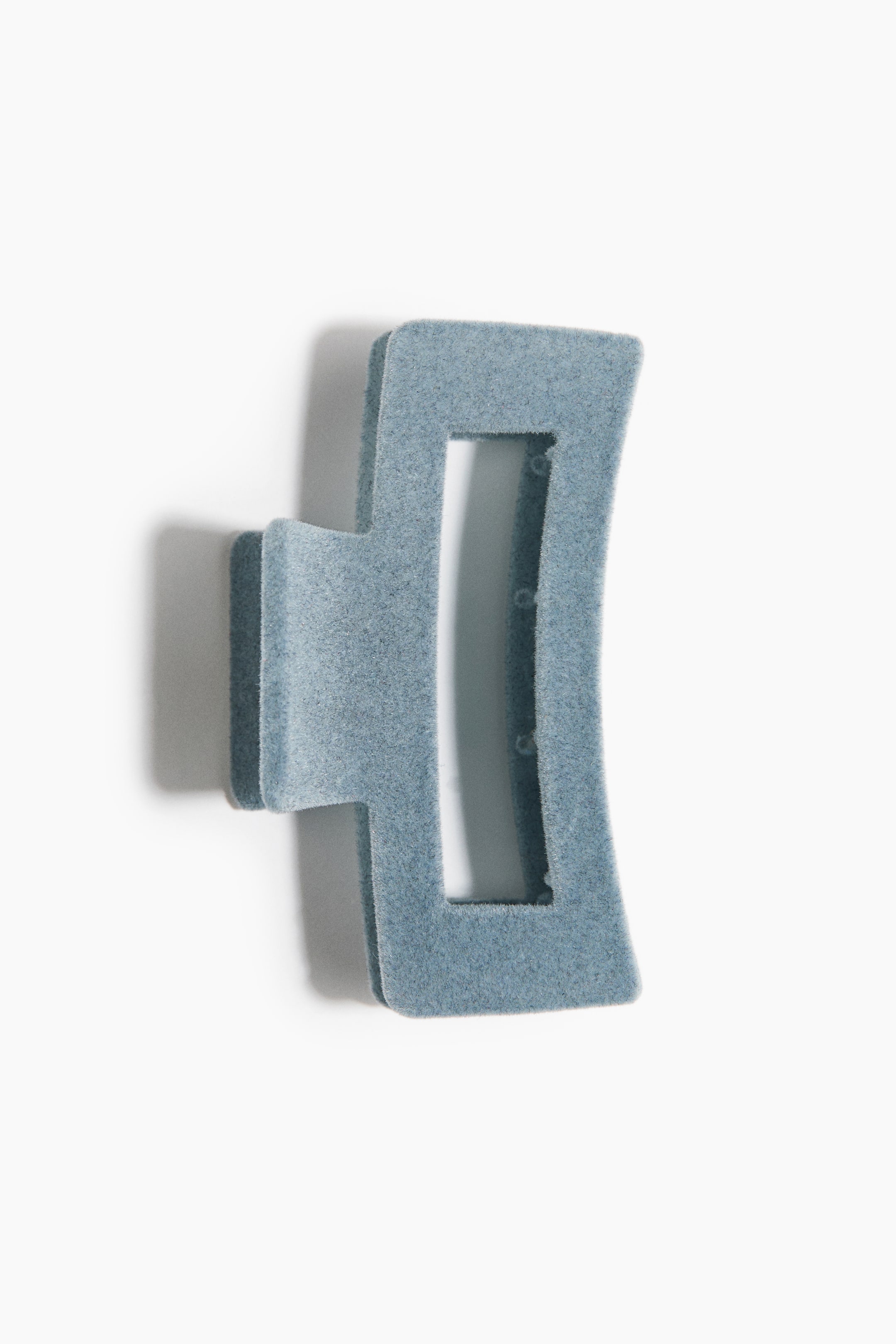 Grotere afbeelding bekijken: Een haarklem wordt gepresenteerd met een stoffigblauwe flockafwerking, met een hoekig, geometrisch ontwerp met afgeronde randen en een centrale rechthoekige opening. Het scharniermechanisme is zichtbaar vanuit een licht schuin aanzicht van voren.