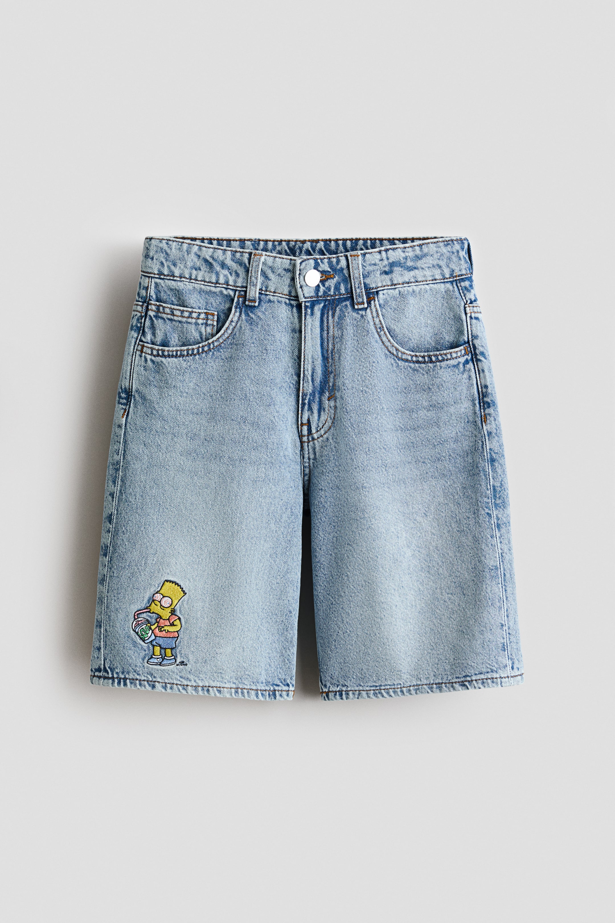 Visualizza l'immagine ingrandita: Shorts in denim azzurro chiaro mostrano una vista frontale, con chiusura a bottone e cerniera in vita, passanti per cintura e tasche anteriori. Un personaggio ricamato di Bart Simpson è visibile sulla parte inferiore della gamba sinistra.
