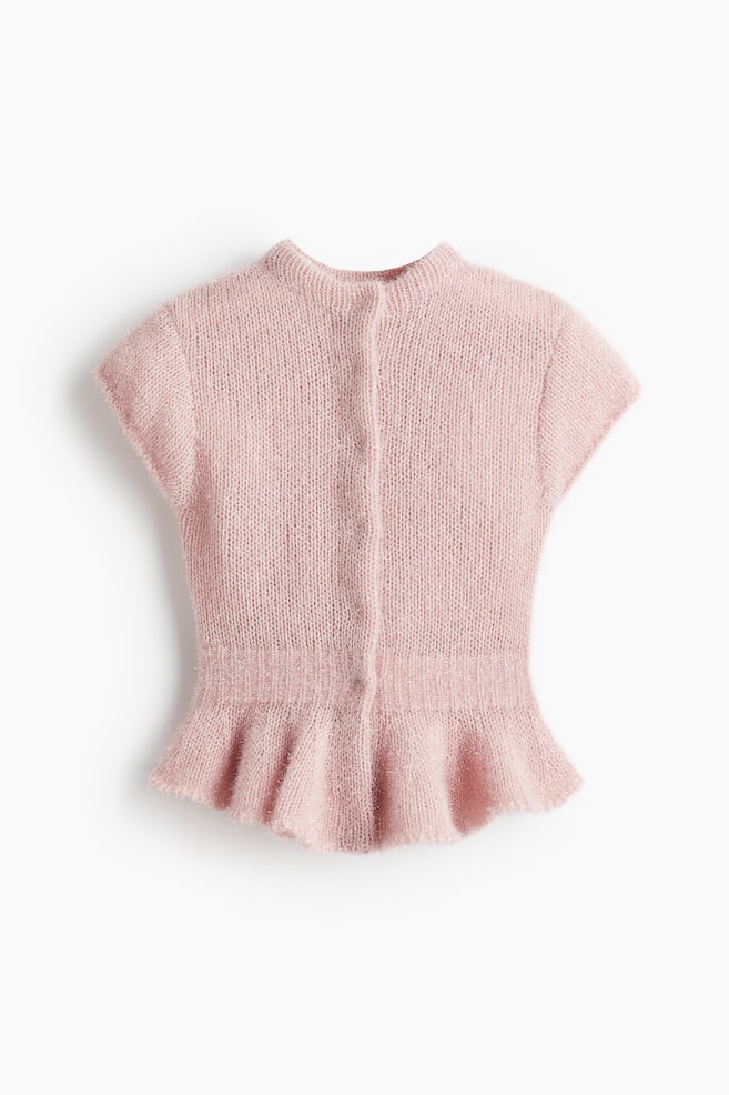 A pink, short, fitted top is being presented FRONT, featuring a fuzzy knit with subtle glossy threads. It is designed with a small stand collar, cap sleeves, a front placket with concealed press-studs, elasticated ribbing at the waist, and an asymmetric peplum hem. - 1