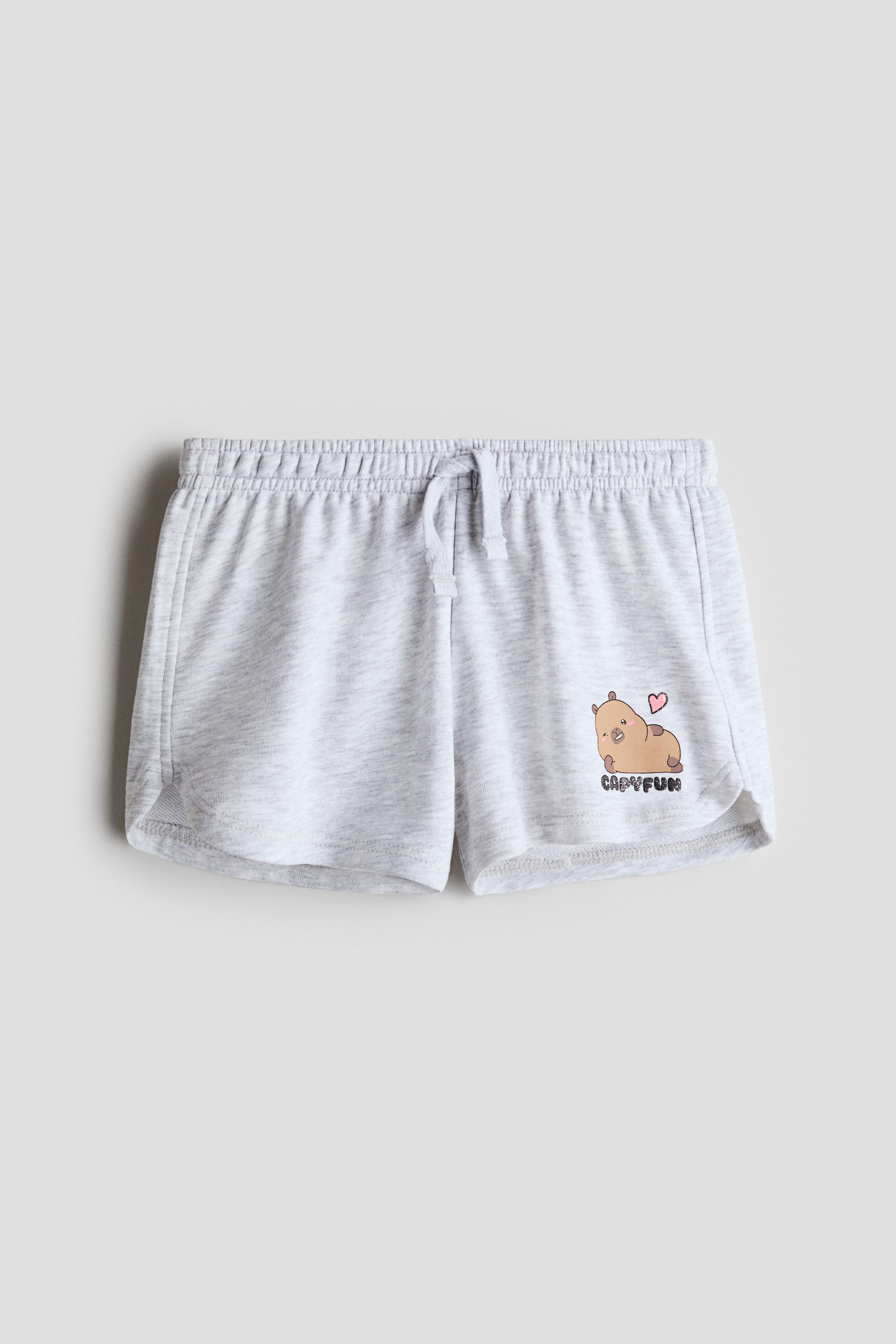 View larger image: The shorts showcase a light grey marl fabric from a front perspective, highlighting an elasticated drawstring waistband at the top. A cartoon capybara graphic with a pink heart and the text "CAPYFUN" is visible on the lower right leg. Noticeable stitching runs along the side seams, while the leg openings feature a curved hemline.
