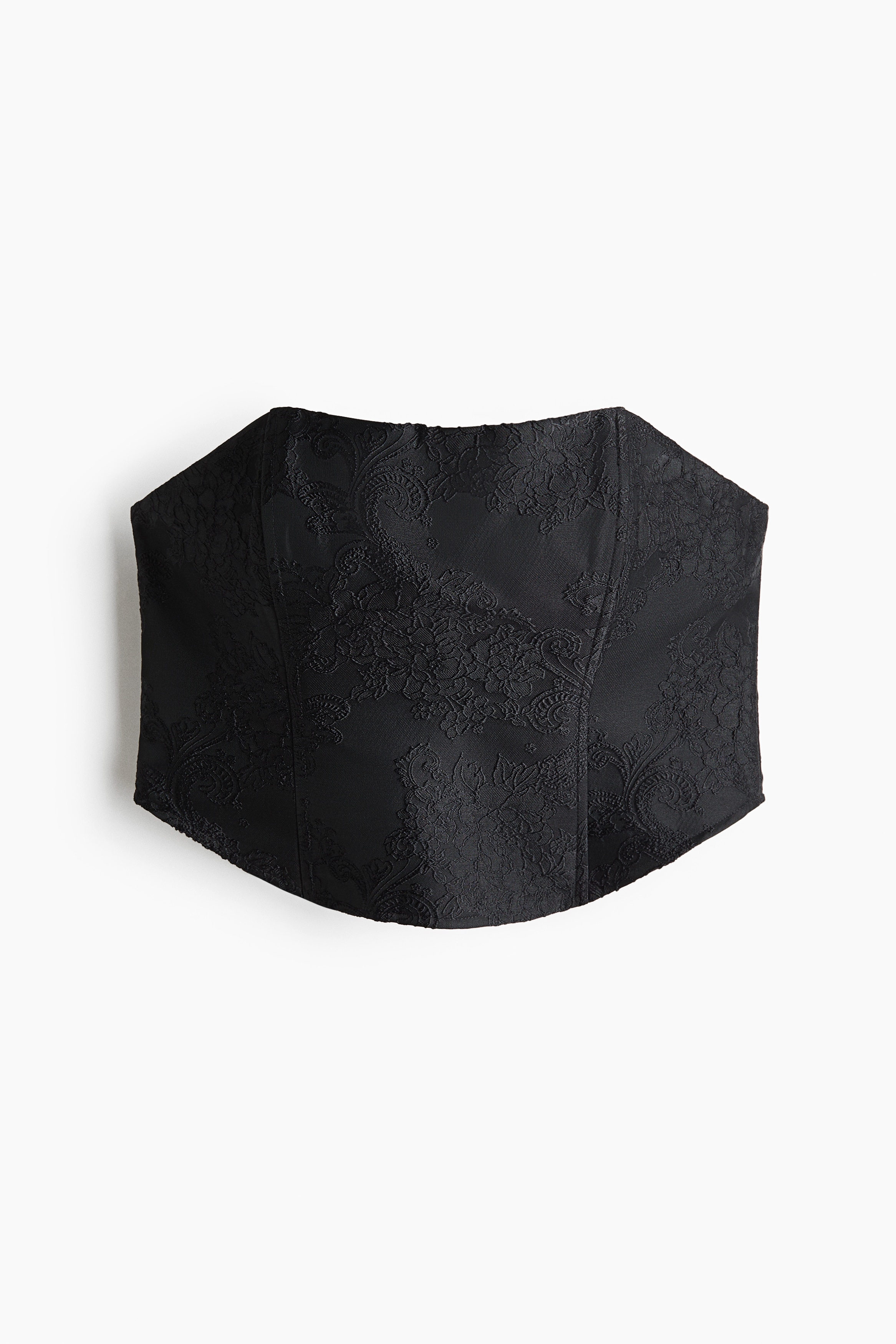 A black cropped bandeau top in a textured jacquard weave is worn by the model, featuring a straight neckline, structured vertical seams and a rounded hem at the front. The top is styled with a matching black jacquard skirt.