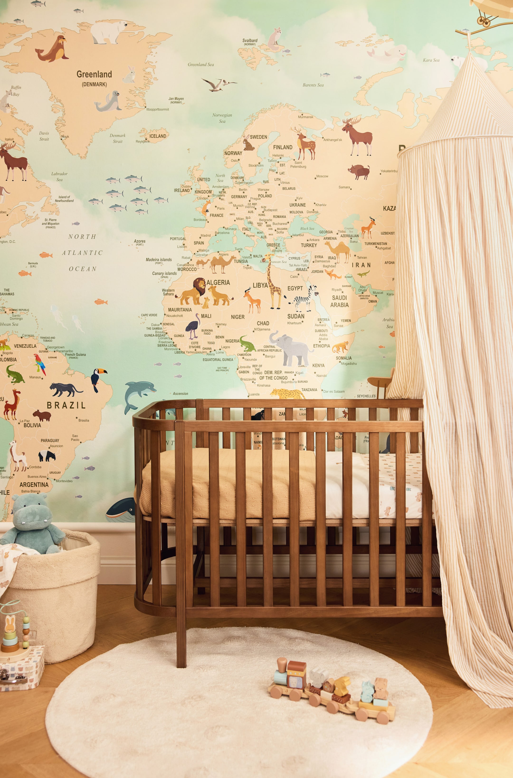 Grotere afbeelding bekijken: Een houten babybedje met een warme walnootafwerking heeft een afgerond rechthoekig frame met verticale spijlen en afgeronde hoeken. Het babybedje wordt getoond vanuit een frontale hoek en is gestyled met een passend matras, een licht dessinhoeslaken en een goudgele deken.
