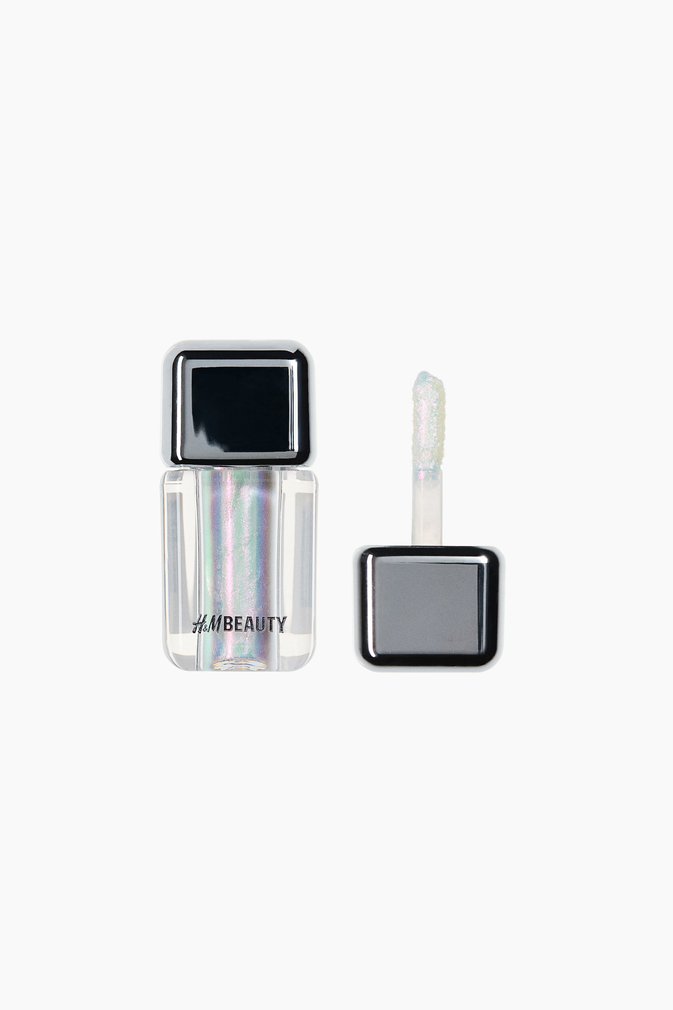 View larger image: A clear rectangular bottle of H&M Beauty shimmery liquid product is standing, showcasing its iridescent contents. Its detached applicator, featuring a shiny black square cap and a brush tip coated with the shimmering product, is resting beside it.