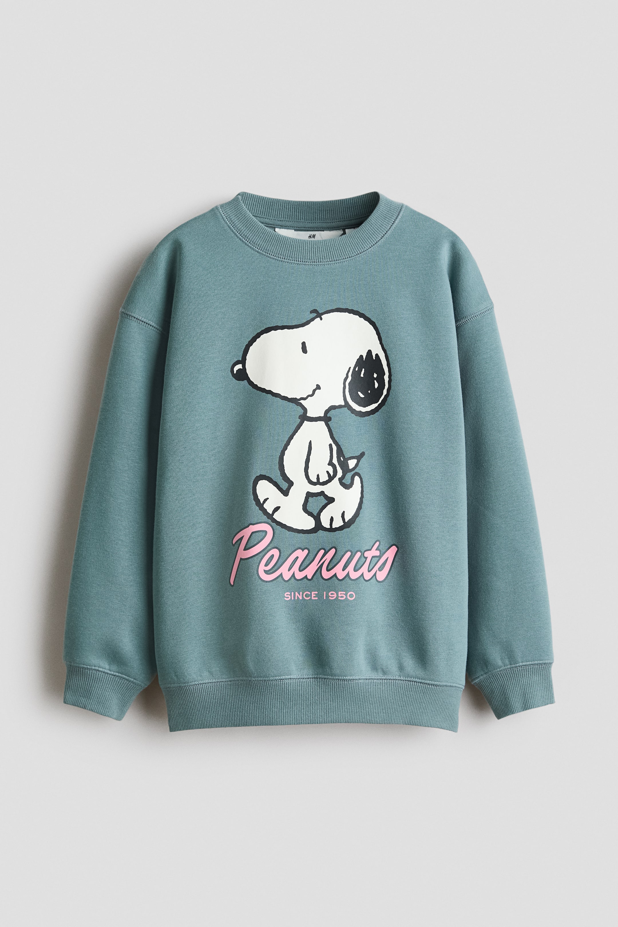 View larger image: A teal sweatshirt showcases a white and black illustration of Snoopy on the front, with "Peanuts" in pink script and "SINCE 1950" printed below. It features a ribbed crew neck, ribbed cuffs, and a ribbed hem.