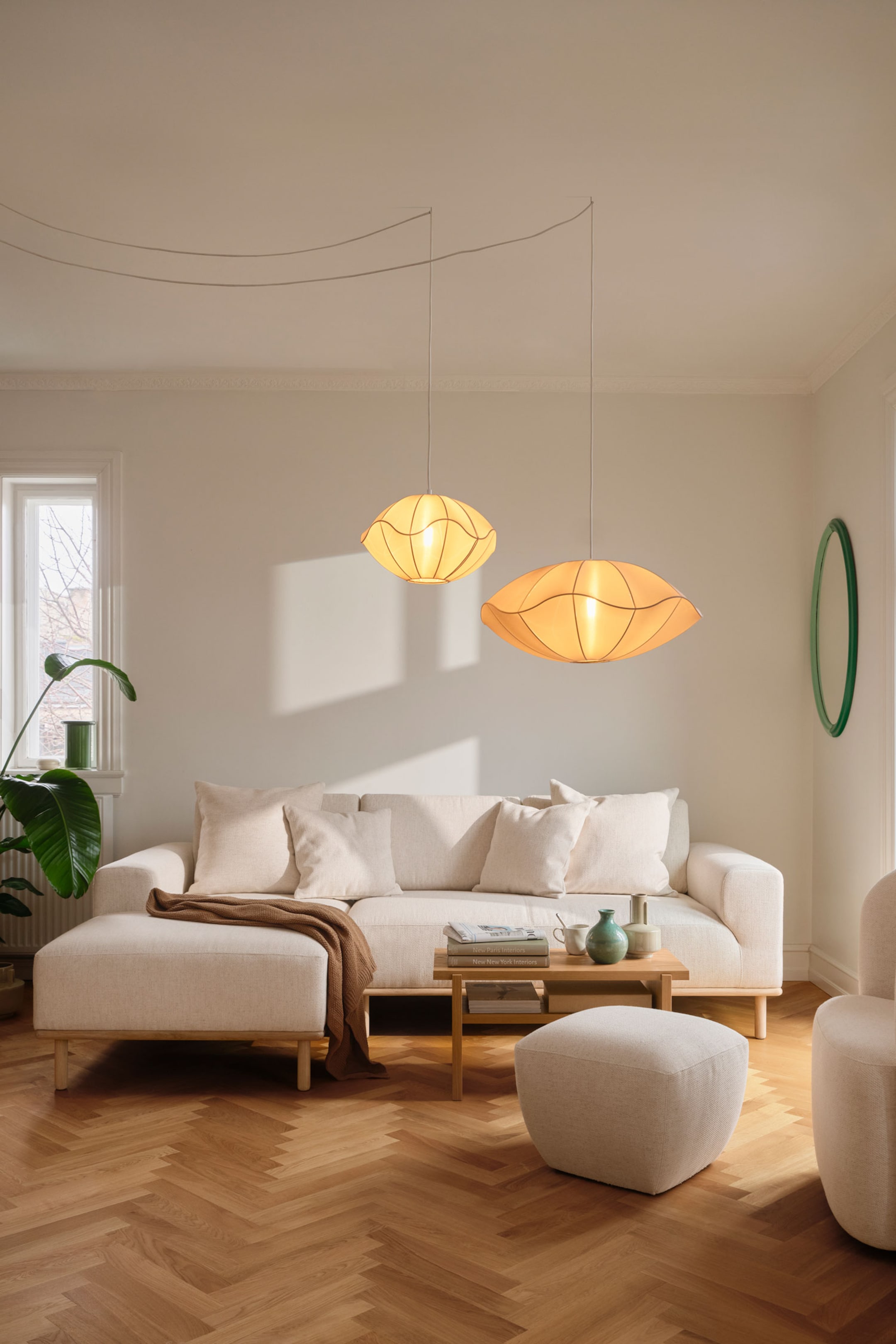 Grotere afbeelding bekijken: Twee hanglampen hangen aan het plafond en hebben brede, schotelvormige lampenkappen van doorschijnende crèmekleurige stof met zichtbare gebogen ribbels. De lampen verspreiden een warme, zachte gloed en hangen op verschillende hoogtes aan dunne witte snoeren.