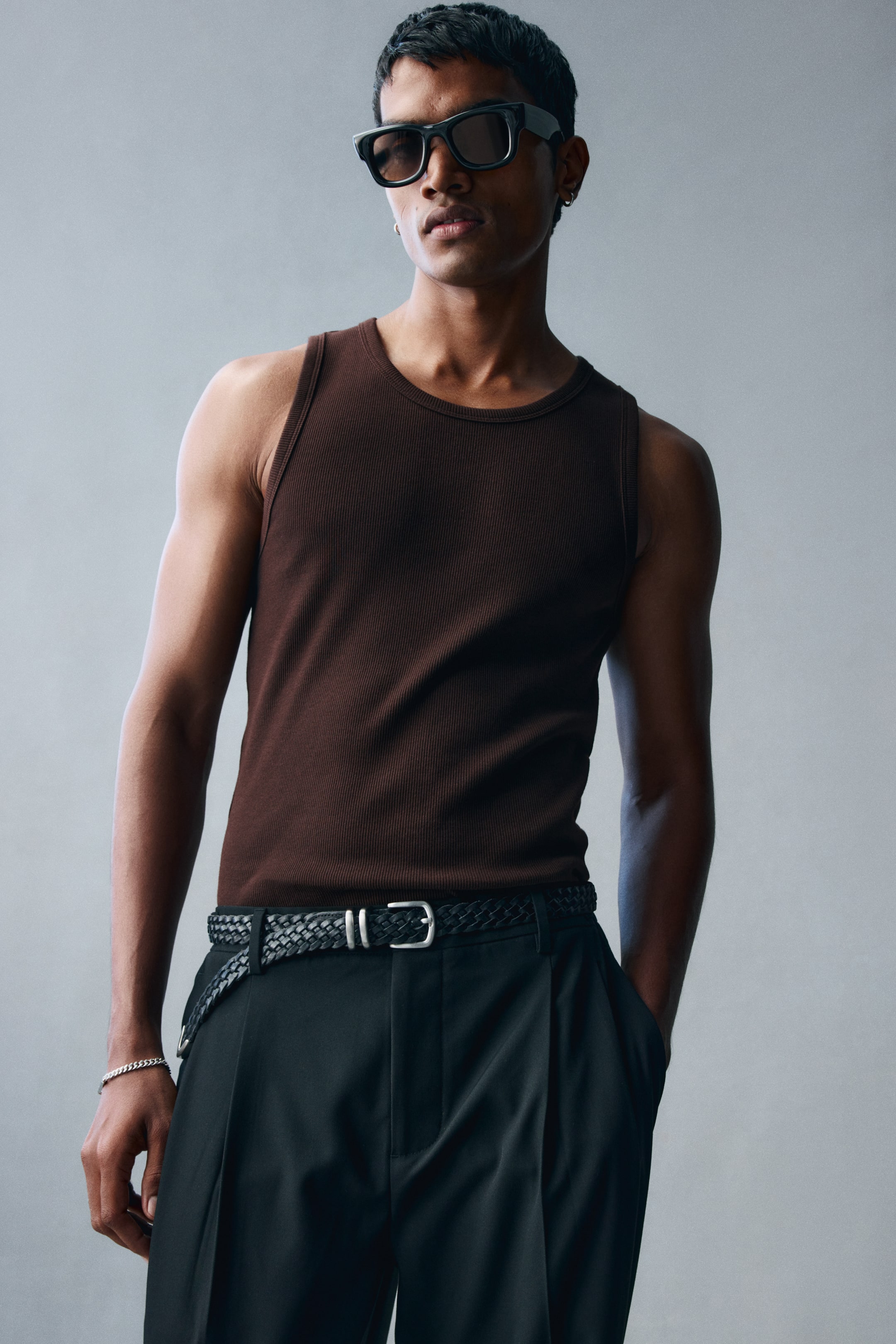 View larger image: A dark brown, ribbed cotton tank top with a round neckline is being worn by the model. The slim-fit tank is tucked into black trousers secured with a braided belt.