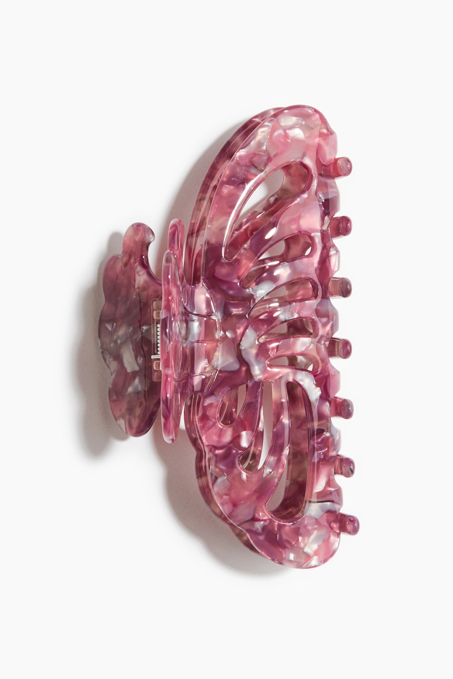 Une pince Ã  cheveux en plastique Ã  la finition brillante prÃ©sente un motif dâailes de papillon ajourÃ©, dans un camaÃ¯eu mouchetÃ© de rose, de violet et de blanc. La pince est montrÃ©e de profil, mettant en valeur ses dents arrondies et incurvÃ©es ainsi que son mÃ©canisme Ã  ressort.
