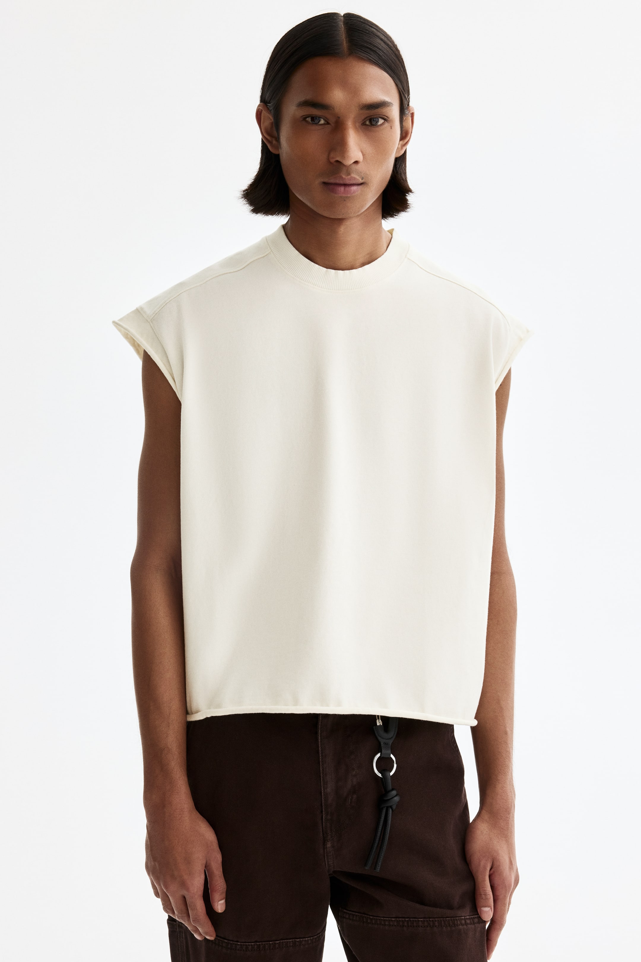 View larger image: An off-white sleeveless top is shown facing forward, featuring a ribbed crew neck and dropped shoulders. Its straight hem shows a raw edge, and it has a relaxed, cropped fit.