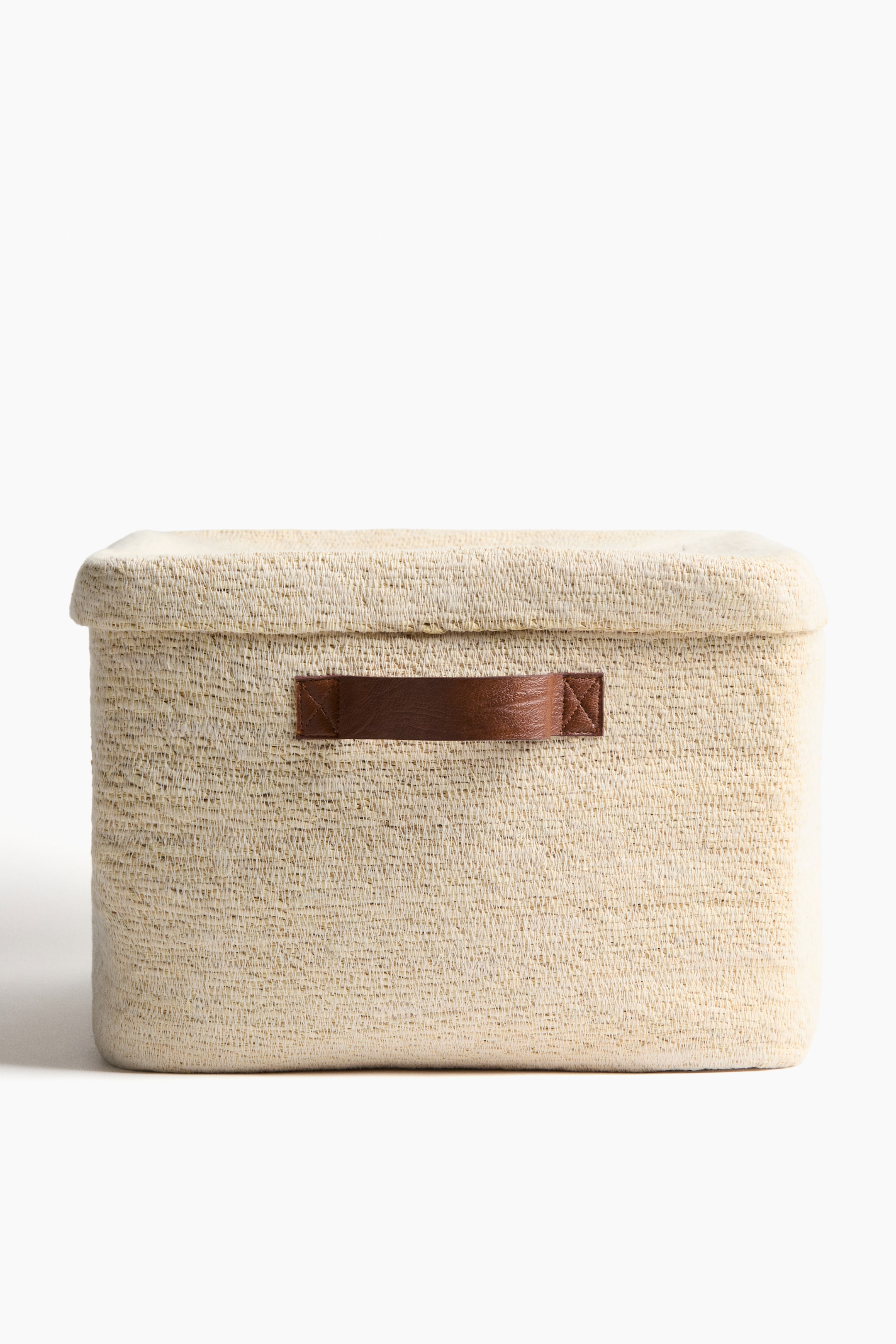 Grotere afbeelding bekijken: Een rechthoekige opbergdoos staat aan de voorkant, en toont zijn licht beige geweven textuur. Het heeft een passend deksel en twee bruine, leerachtige handgrepen aan de voorkant.