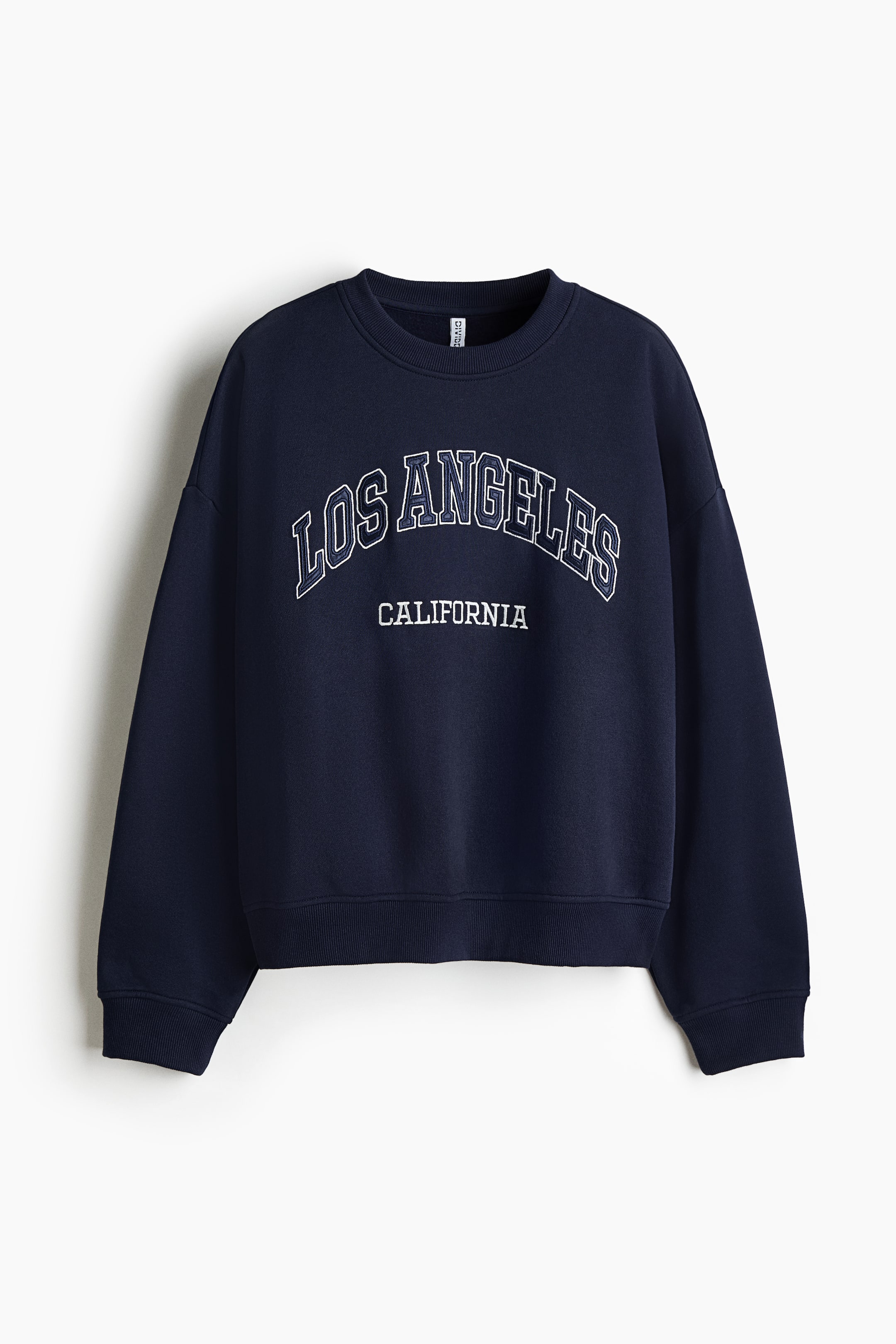 View larger image: A navy blue oversized sweatshirt is shown from the front, featuring a ribbed crew neck, dropped shoulders, and ribbed cuffs and hem. The chest is printed with a collegiate-style graphic reading "LOS ANGELES" in arched letters and "CALIFORNIA" in smaller block letters below.