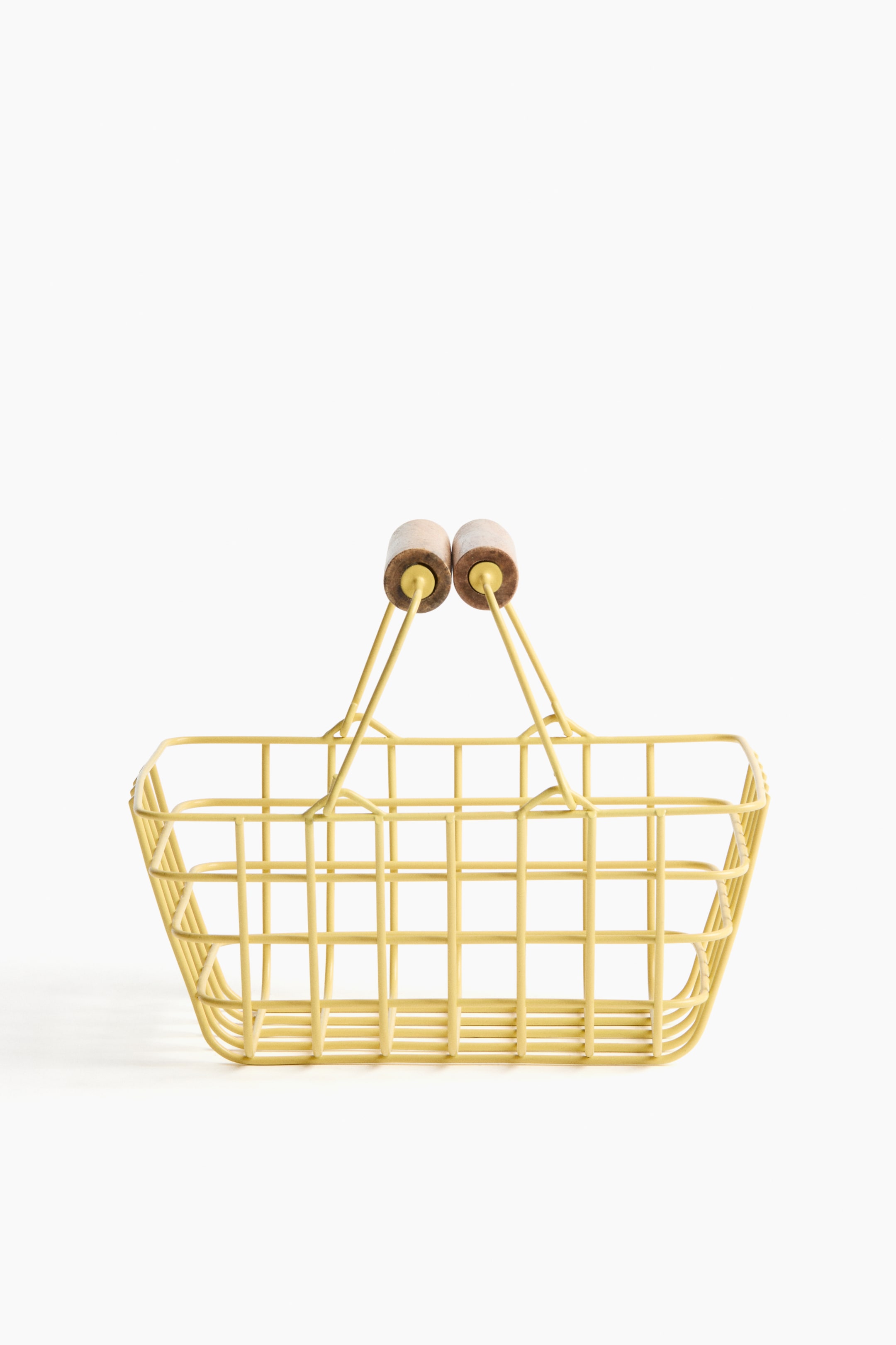 Visualizza immagine più grande: Un cestino porta-spesa in filo dallo stile vintage è rivolto frontalmente. È realizzato con filo metallico di colore giallo chiaro che forma un motivo a griglia quadrata, e due manici in filo si alzano dai lati, ciascuno sormontato da un'impugnatura cilindrica in legno marrone chiaro.