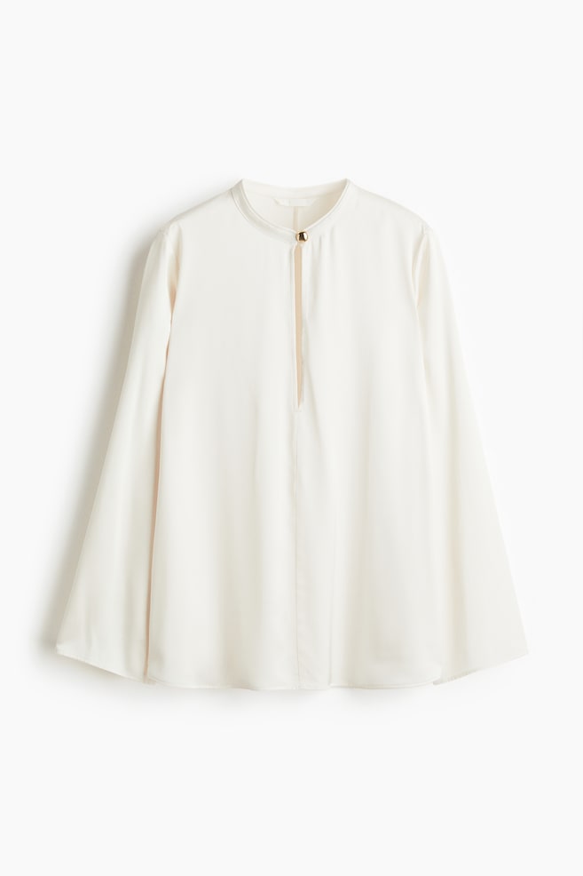 A front view of an off-white blouse is showing a band collar and a front keyhole opening, which is secured by a single gold-toned button. The blouse is designed with long, wide sleeves and a relaxed, flowy silhouette. - 1