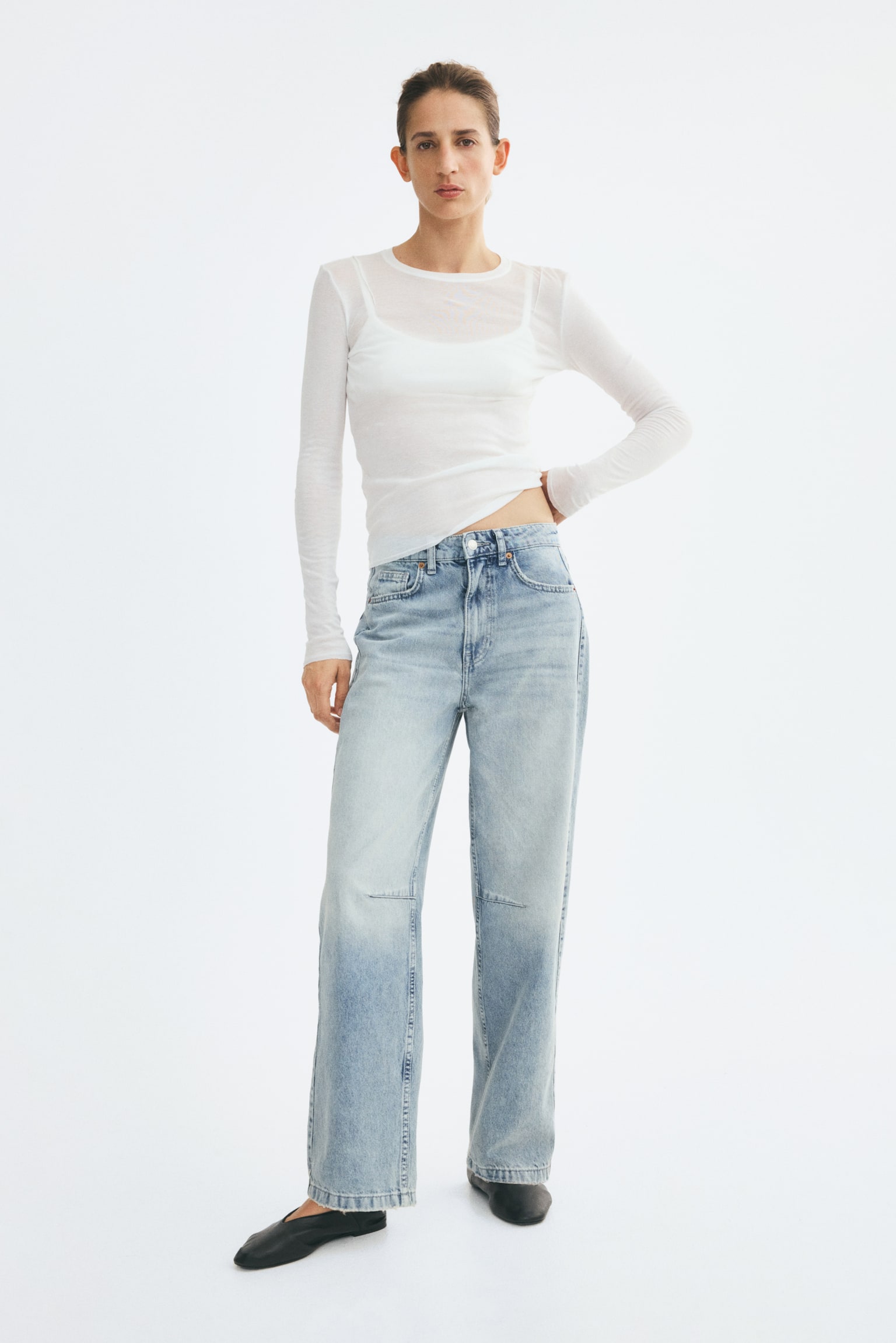 Hell gewaschene Denim-Jeans mit hoher Taille, lockerem Schnitt und geradem Bein werden vom Model getragen. Die Jeans mit klassischer Five-Pocket-Konstruktion sind mit einem transparenten weiÃen Langarm-Top und schwarzen flachen Schuhen kombiniert. - 1