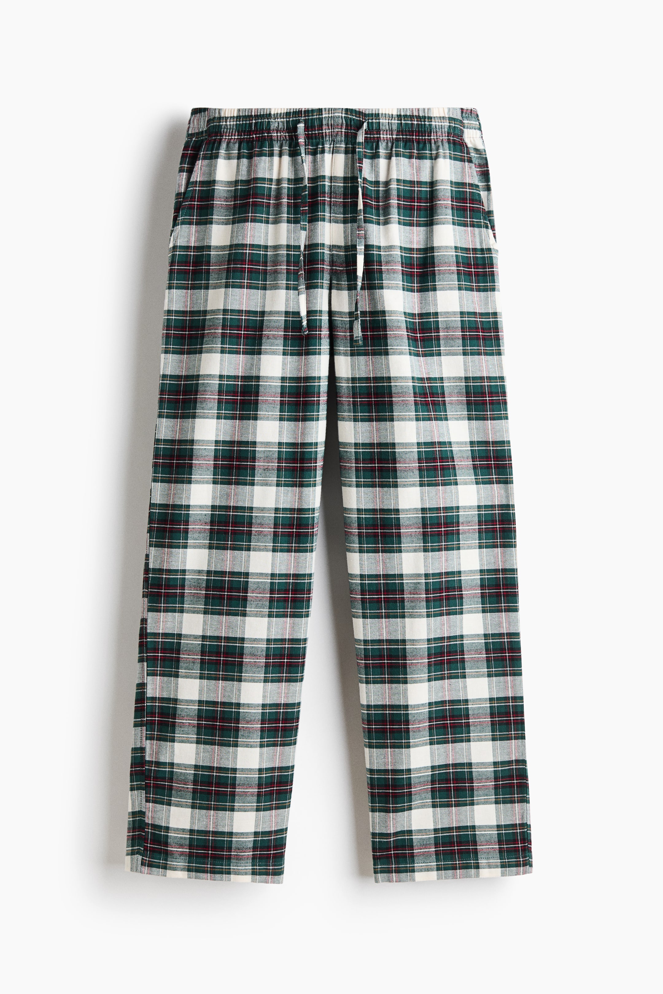 Xem ảnh lớn hơn: Một chiếc quần flannel kẻ sọc đôi màu xanh lá, trắng và đỏ đang được treo ở góc chụp chính diện, thể hiện phom dáng rộng thoải mái với cạp chun có dây rút, khóa giả phía trước và túi chéo hai bên.