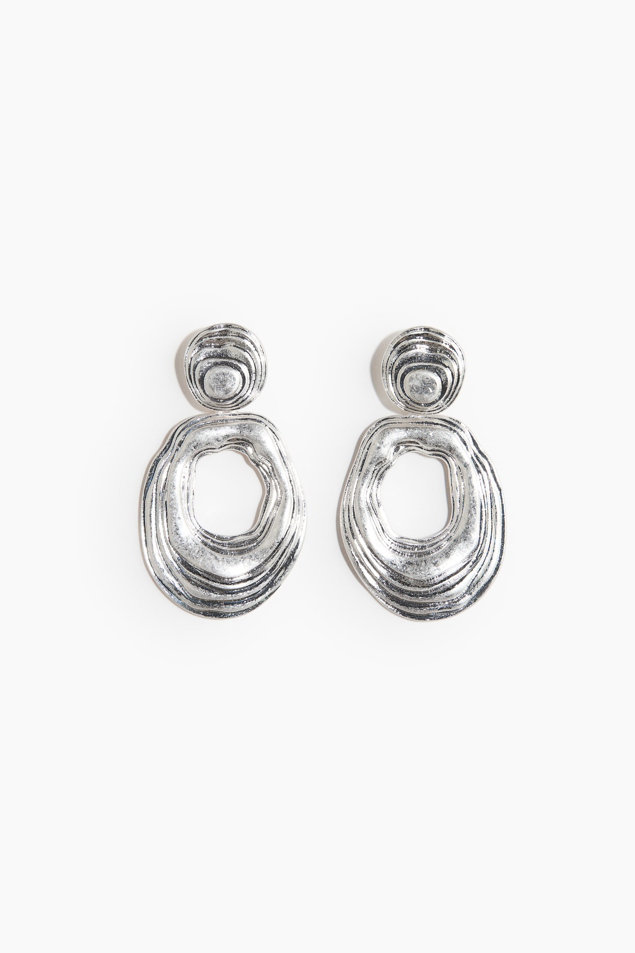 View larger image: A pair of silver-toned dangle earrings is displaying an organic, textured design, presented facing FRONT. Each earring is featuring a rounded stud with irregular concentric grooves, connecting to a larger, irregularly shaped open ring with matching wavy textures.