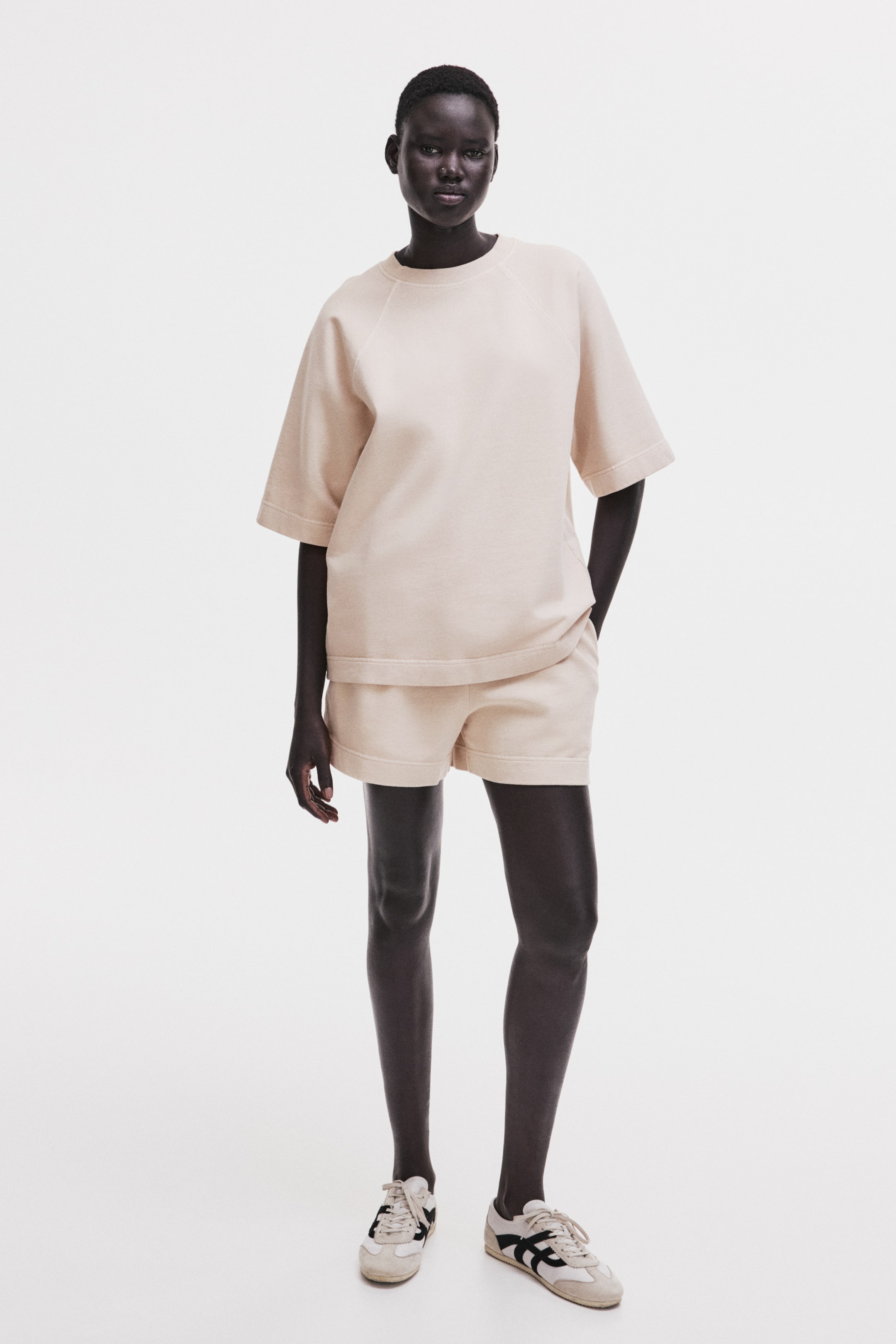 View larger image: A light beige matching set is shown, consisting of a crew-neck top and loose shorts. The top features short raglan sleeves and a wide, straight hem, while the shorts also have a straight hem and pockets.