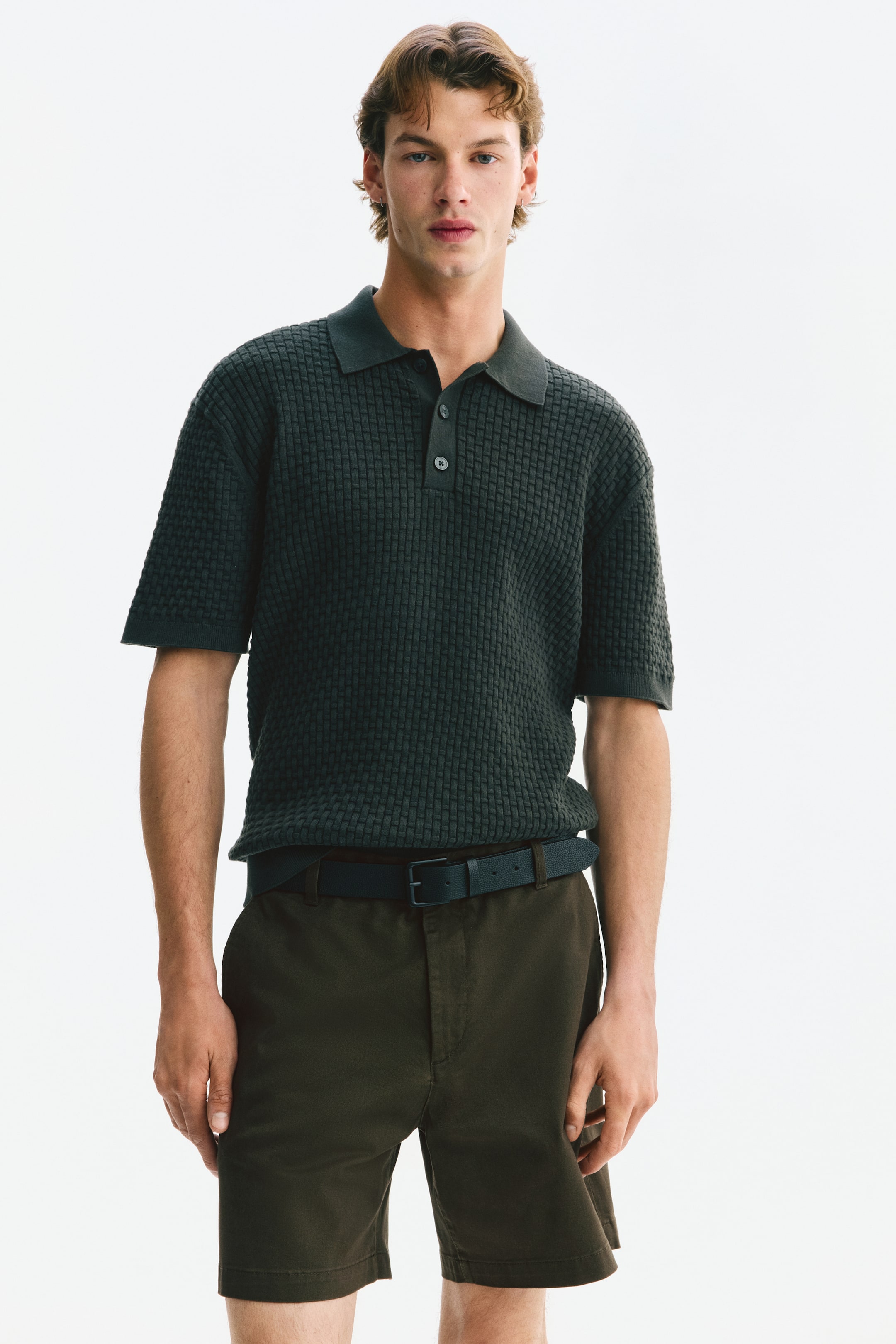 Größeres Bild anzeigen: Dunkelolivfarbene Chino-Shorts aus Baumwolltwill werden vom Model getragen, mit Knopfverschluss und vorderen Tascheneingriffen. Ein dunkler Gürtel wird zu den regular fit Shorts getragen.