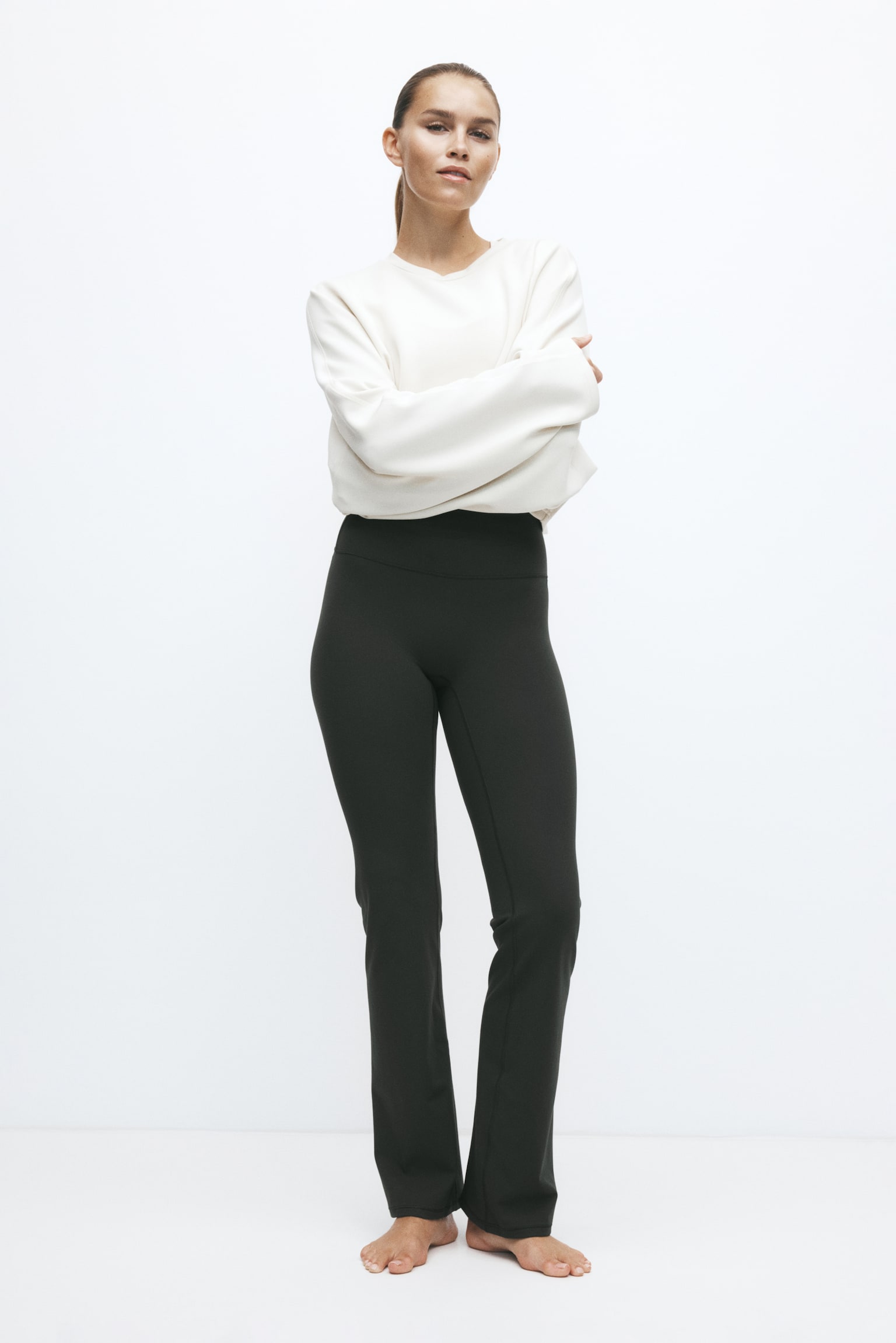The model is wearing black high-waisted trousers with a wide waistband and a slightly flared leg, styled with a cream-coloured long-sleeved sweatshirt. - 1