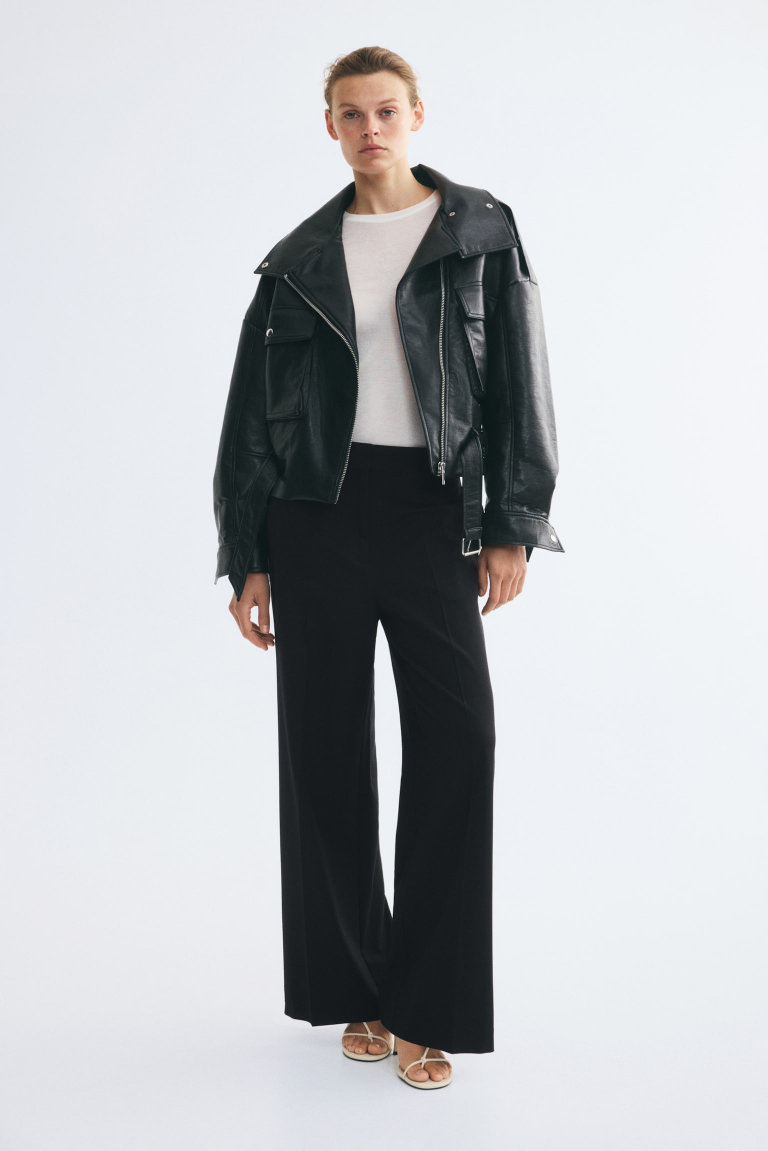 Front view of black tailored trousers in woven fabric, featuring a high-waisted fit, a visible zip fly, subtle side pockets and wide legs with prominent creases running down the front. - 1