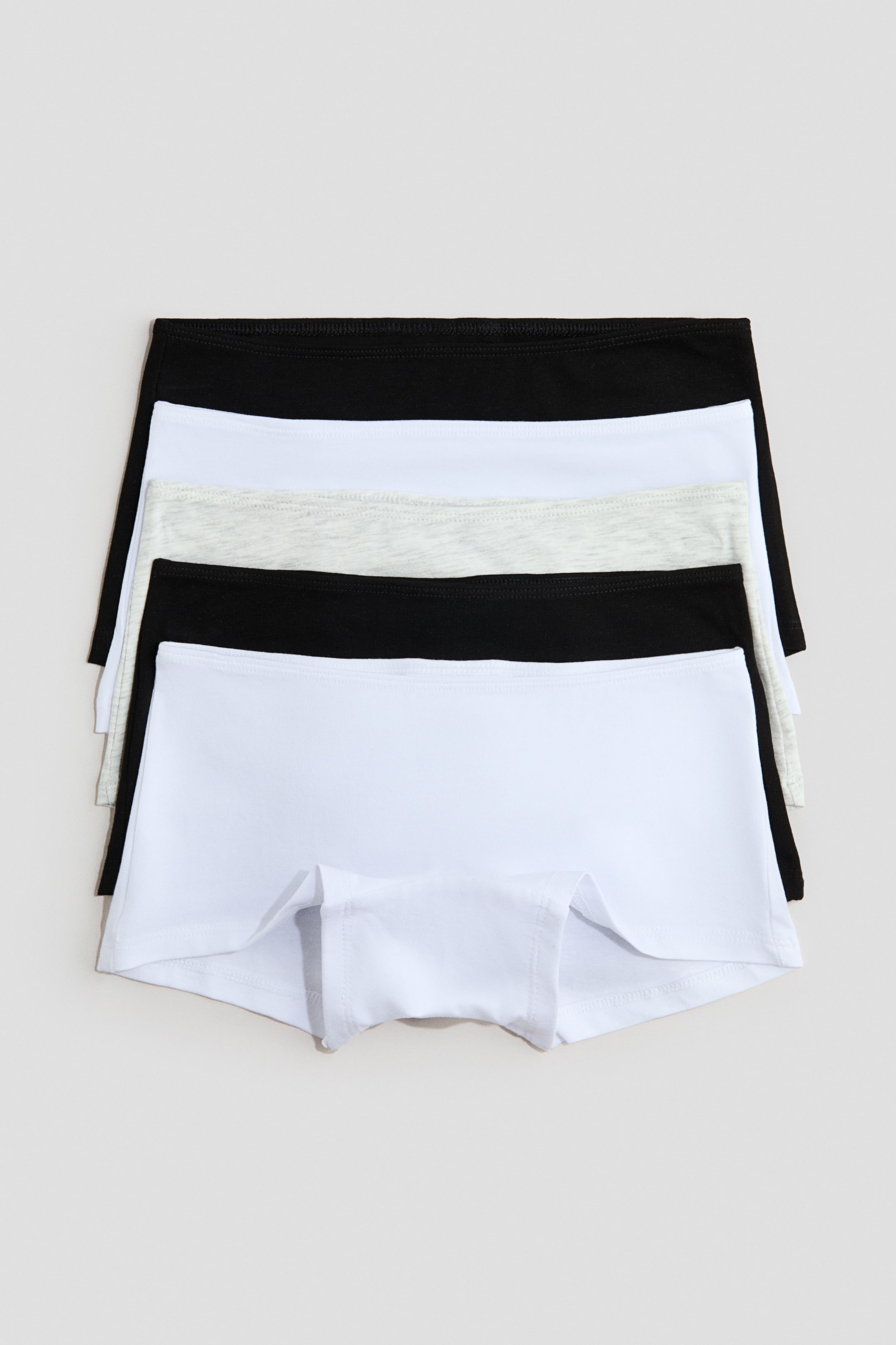 View larger image: Five pairs of boy short underwear are displayed in a stack, showcasing alternating black, white, and light grey marl colours. The bottom white pair is facing front, clearly revealing its leg openings and centre front panel.