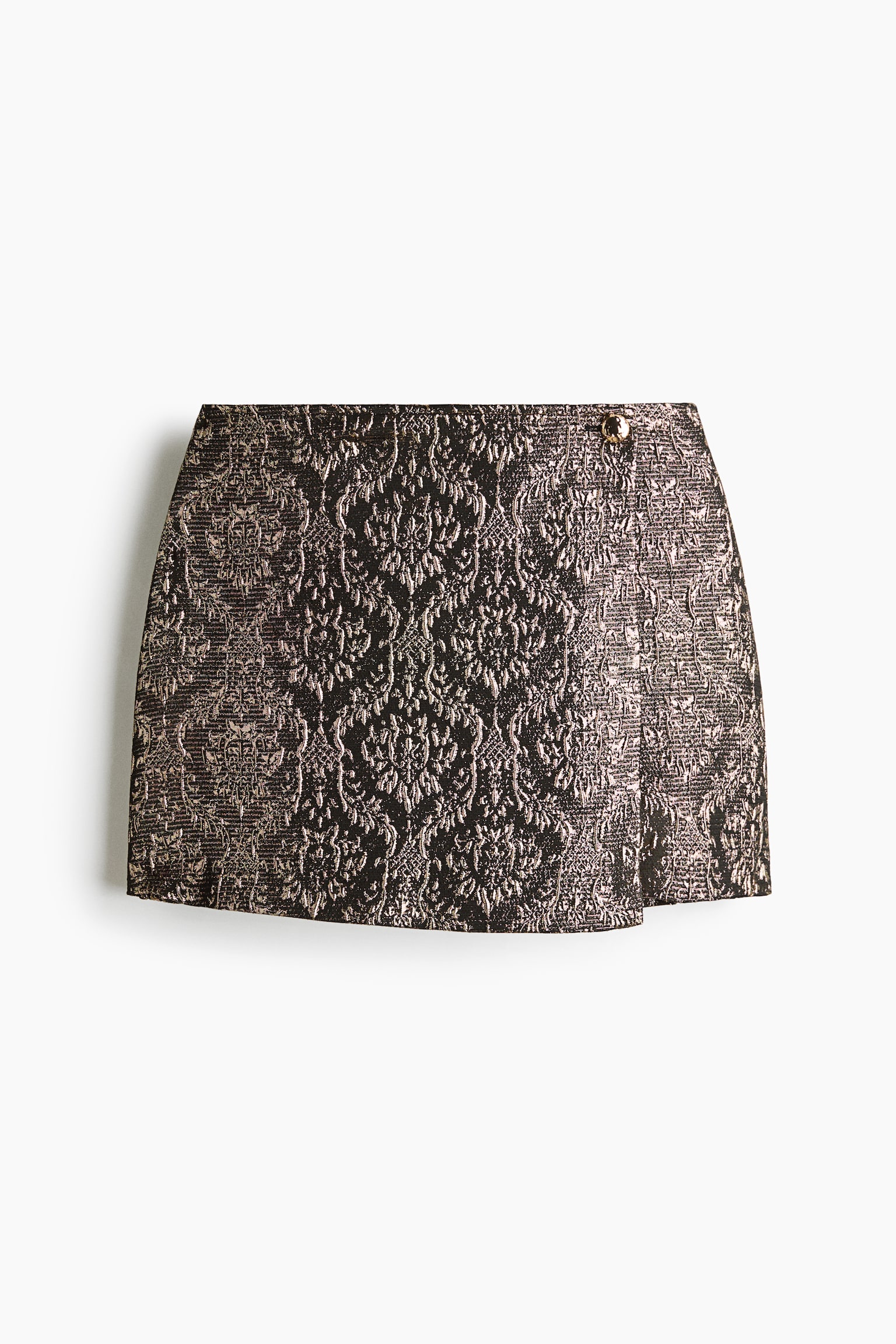 A metallic brocade wrap mini skirt is shown from the front, displaying an intricate bronze and black damask pattern. The skirt features an overlapping front panel secured by a single gold button at the waistband, creating a structured A-line silhouette.