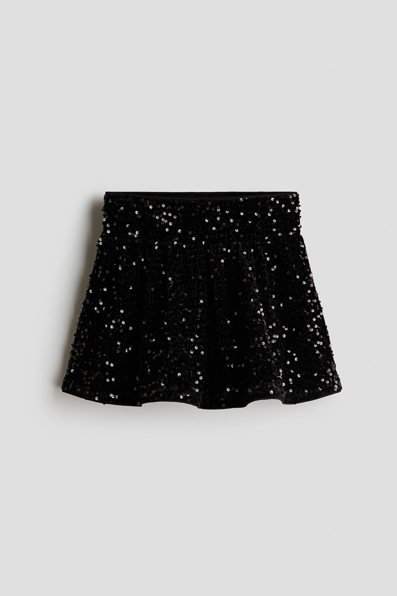 A black sequinned skirt is shown from the front, displaying an A-line silhouette covered in shimmering black sequins. The skirt features a flat waistband and a flared, wavy hem.