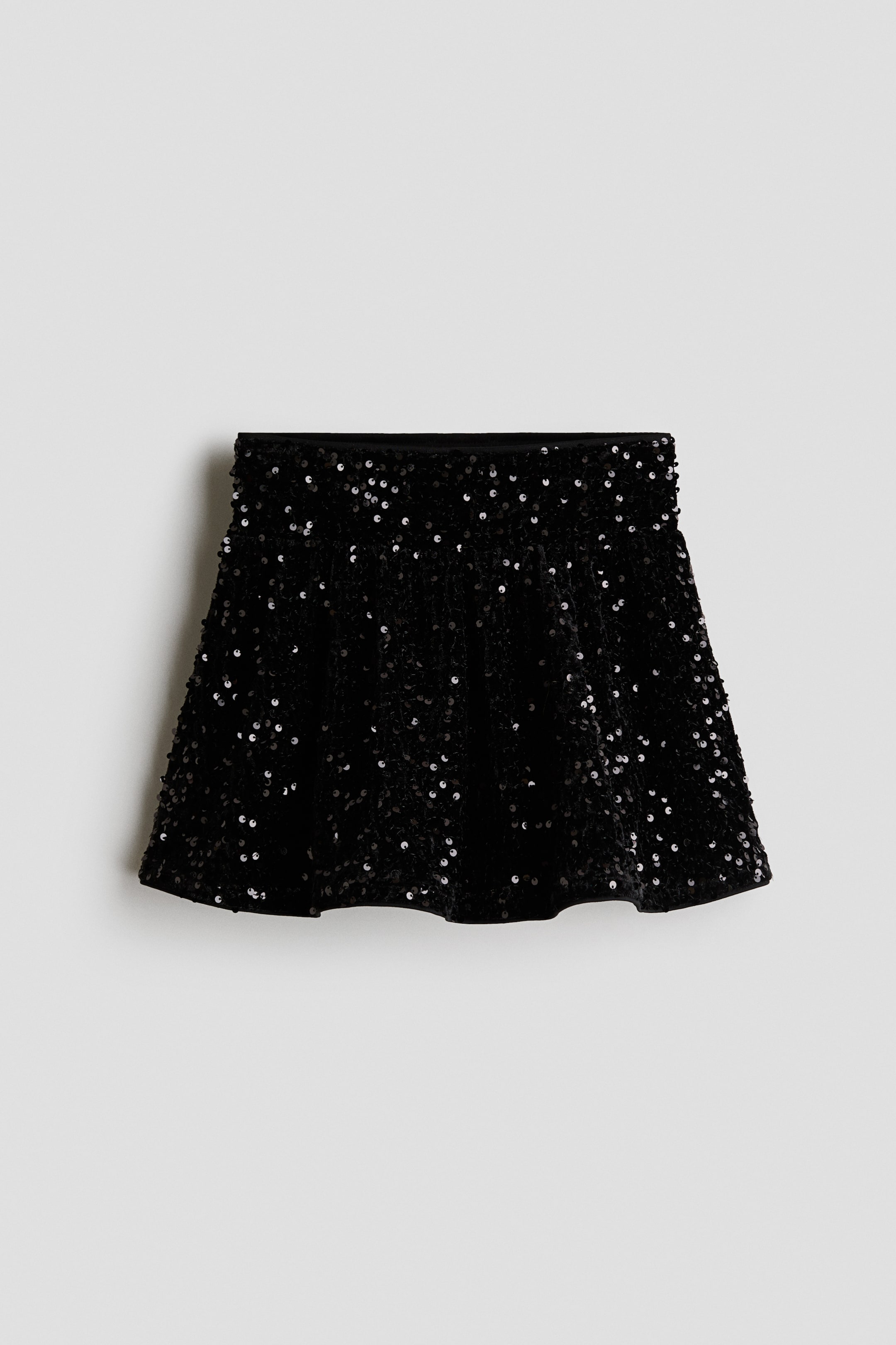 View larger image: A black sequinned skirt is shown from the front, displaying an A-line silhouette covered in shimmering black sequins. The skirt features a flat waistband and a flared, wavy hem.