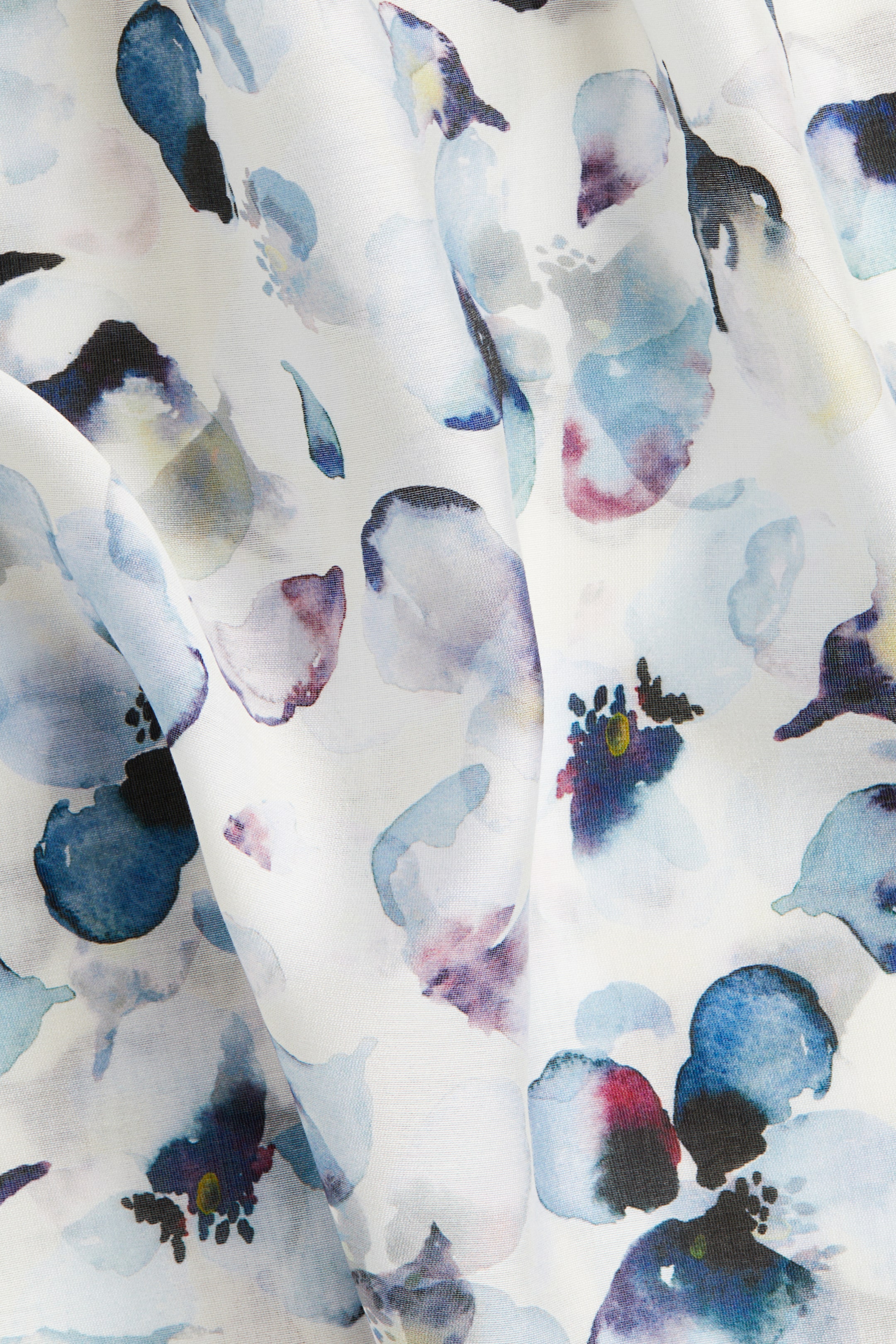 View larger image: A fabric is featuring an abstract floral watercolor pattern in shades of blue, purple, and hints of pink on a white ground. It is softly draped, revealing flowing folds.
