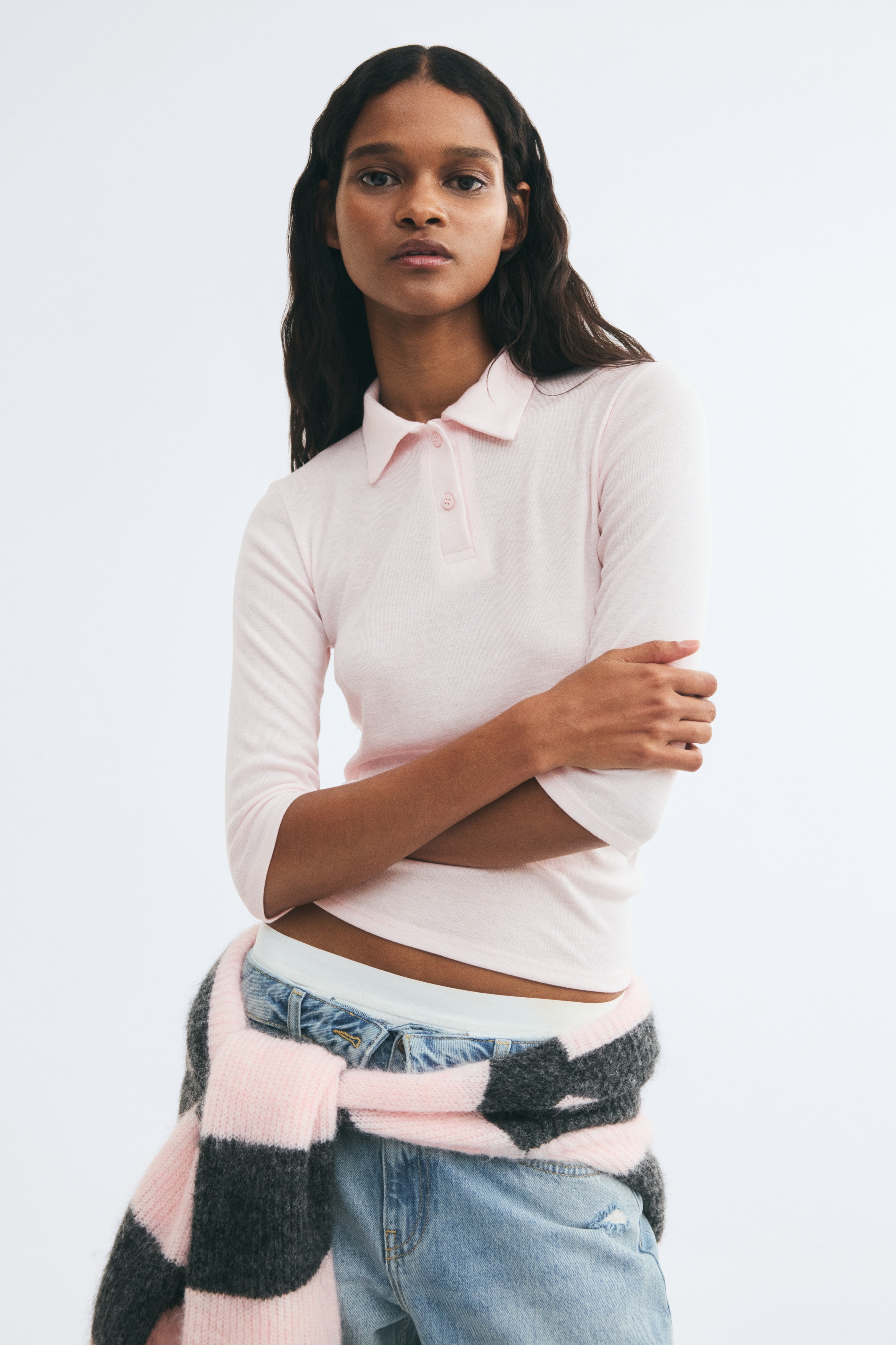 Una polo rosa chiaro in jersey a costina fine Ã¨ mostrata frontalmente, con un colletto classico, una chiusura con due bottoni e maniche a tre quarti. La camicia Ã¨ progettata con un orlo diritto, presentando una silhouette pulita e semplice.