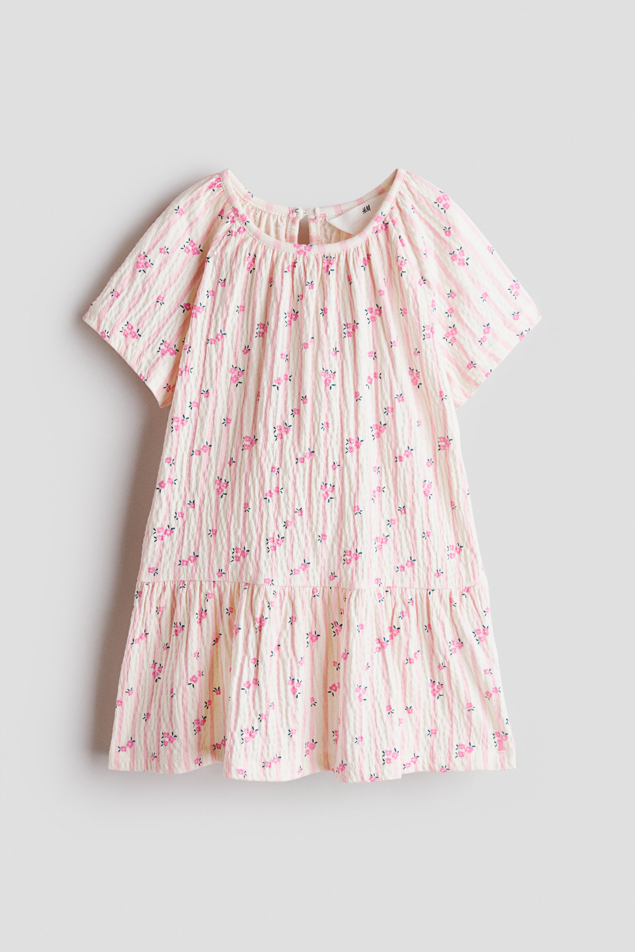 Ver imagen más grande: Un vestido confeccionado en punto de algodón ligeramente texturizado luce un estampado de rayas rosas y pequeños motivos florales rosas. Presenta un escote redondo con frunces alrededor, mangas raglán cortas, una abertura tipo lágrima con botón en la nuca y una falda evasé con costura fruncida por encima del bajo para aportar mayor volumen.
