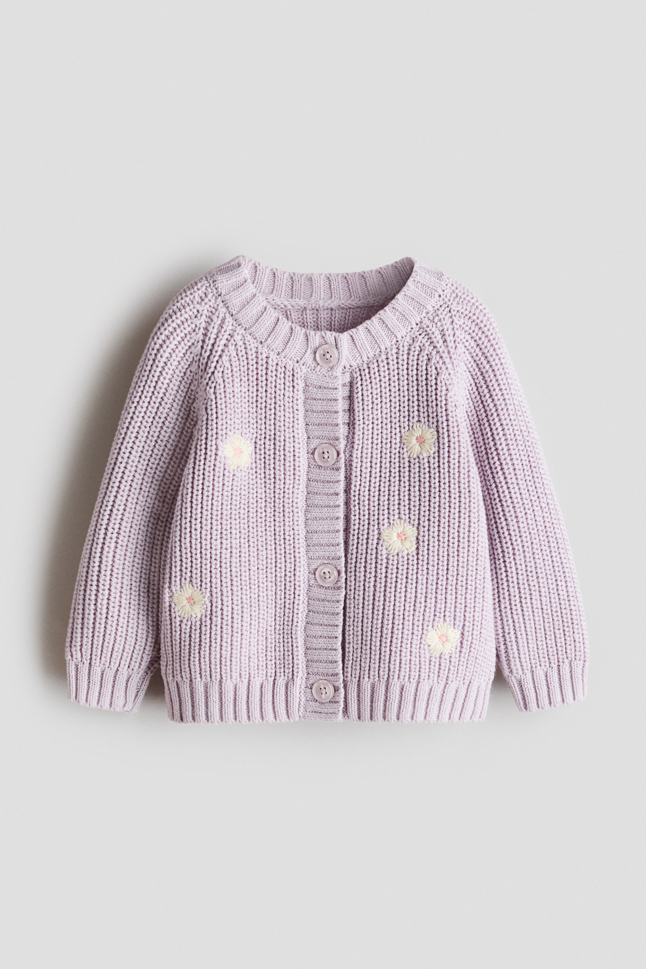 View larger image: A lavender knitted cardigan is showcasing its front, featuring a chunky ribbed texture, long raglan sleeves, ribbed cuffs, and a ribbed hem. It boasts a round neck and a front button-up fastening with five matching buttons, adorned with scattered white and yellow embroidered daisy flowers across the body and sleeves.