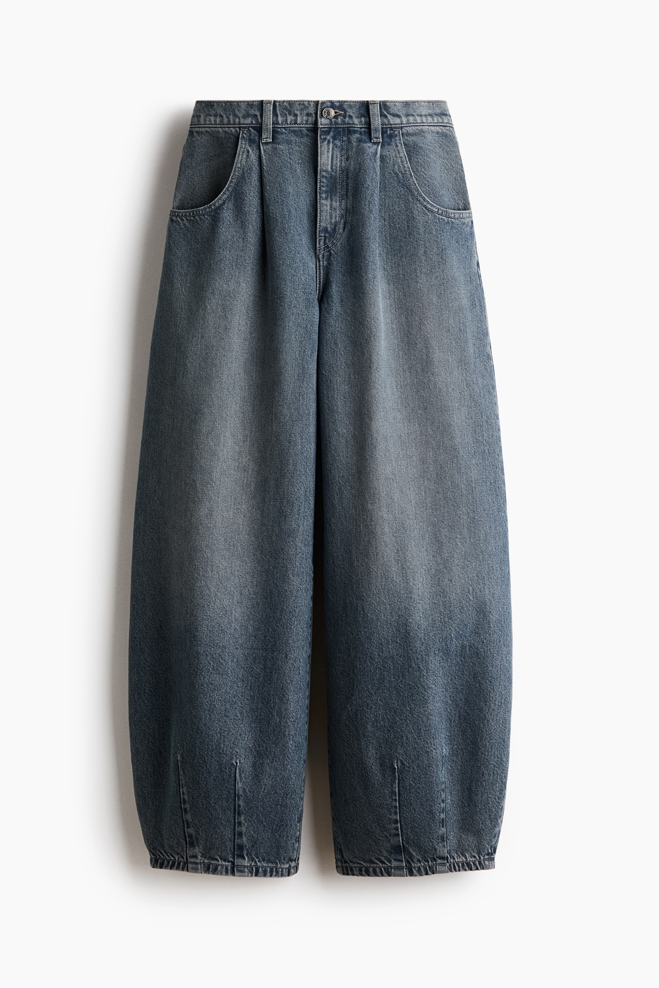 View larger image: A pair of blue denim jeans is shown from the front, featuring a curved, voluminous leg silhouette that tapers toward the hem with vertical darts. The jeans showcase a faded blue wash, front pleats, scoop pockets, and a regular waist with a button and zip fly closure.