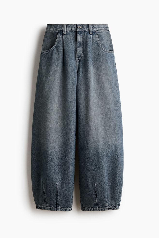 Ein Paar blaue Denim-Jeans wird von vorne gezeigt und zeichnet sich durch eine geschwungene, voluminöse Beinsilhouette aus, die zum Saum hin mit vertikalen Abnähern schmaler wird. Die Jeans zeigt eine verwaschene blaue Waschung, Frontfalten, Eingrifftaschen und eine reguläre Taille mit Knopf- und ReiÃverschluss. - 1