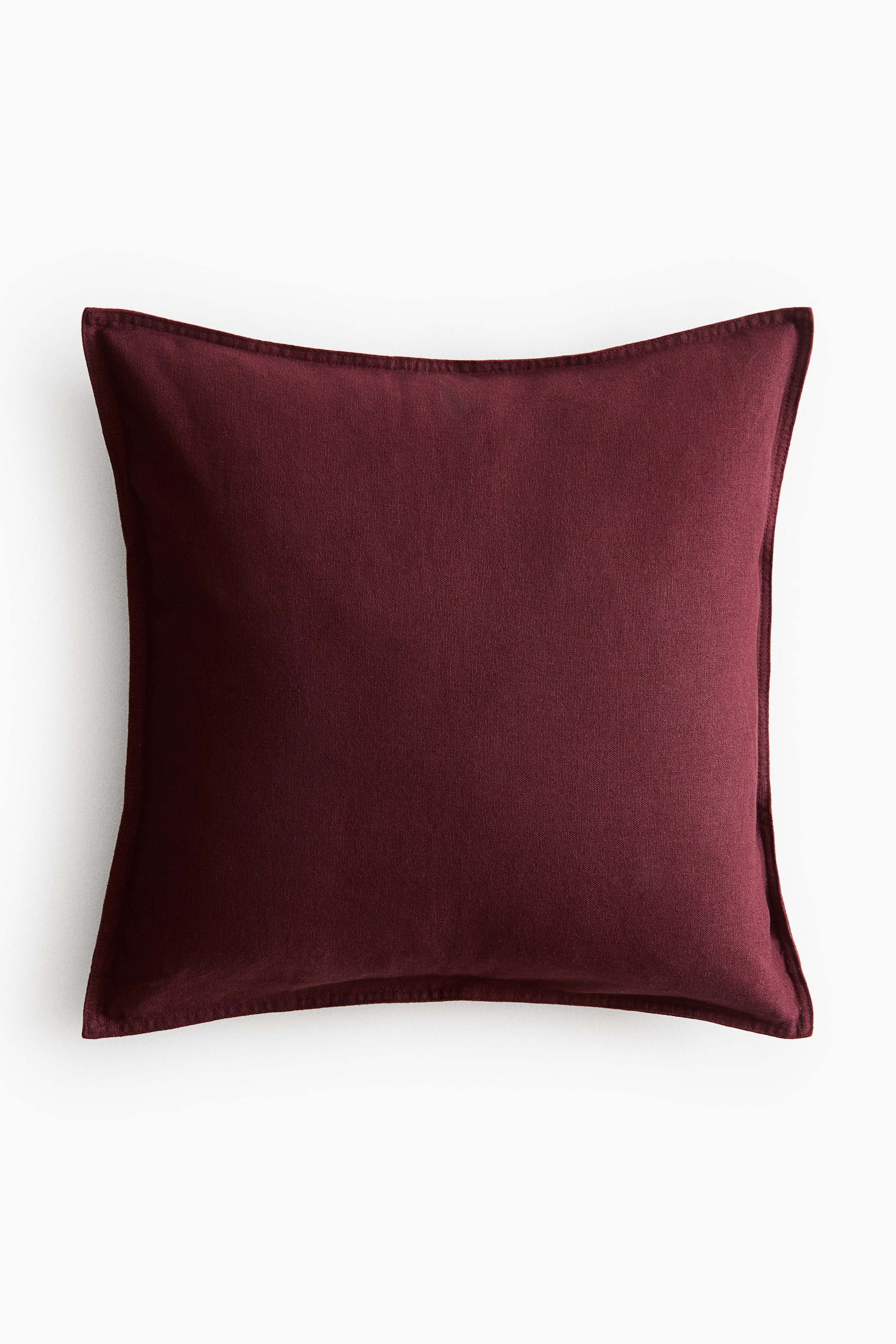 View larger image: The deep red cushion cover features a linen and cotton weave with visible stitching along its sides.