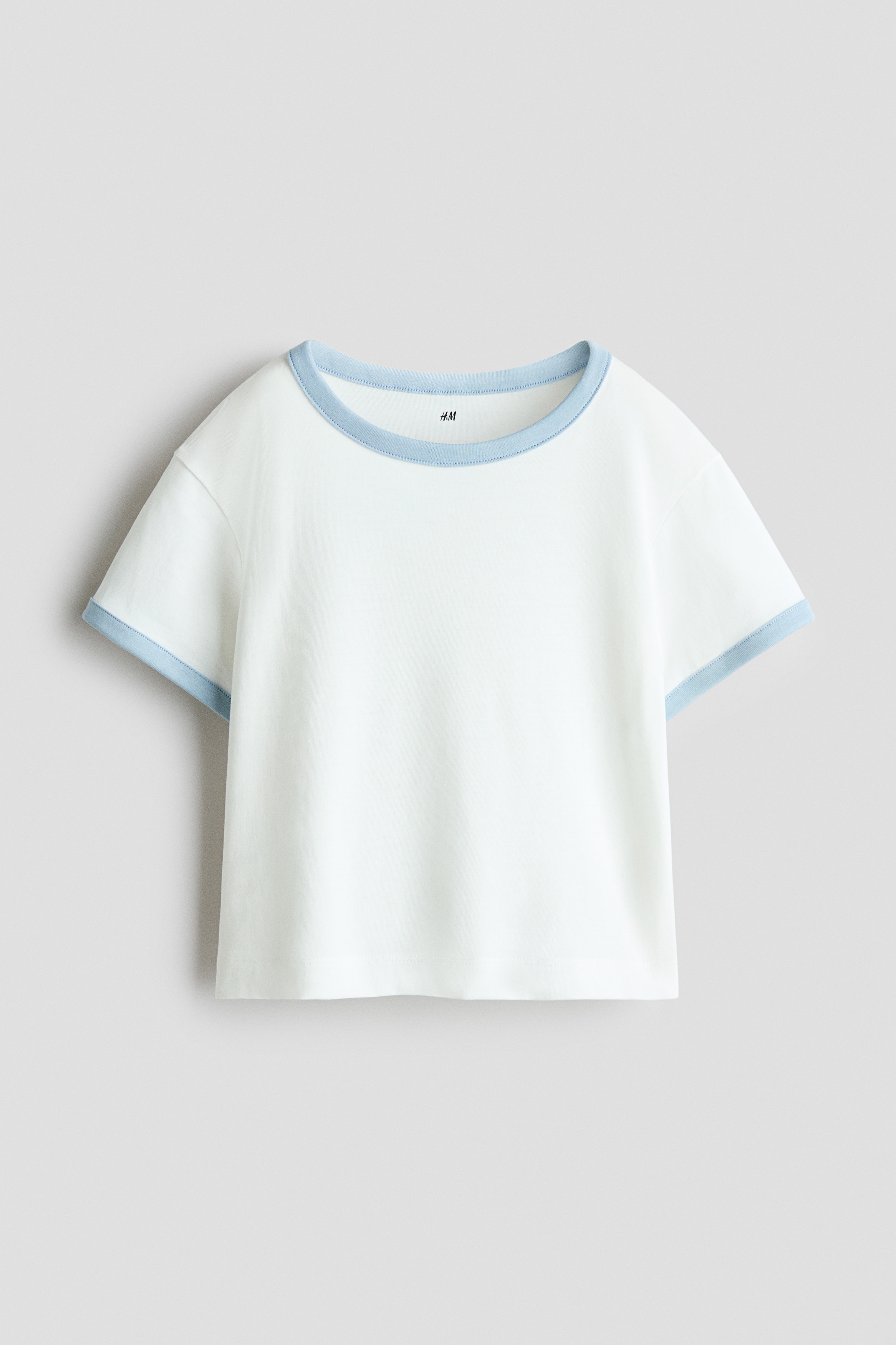 The model is wearing a white short-sleeved ringer t-shirt with light blue trim on the collar and cuffs, paired with matching light blue shorts.