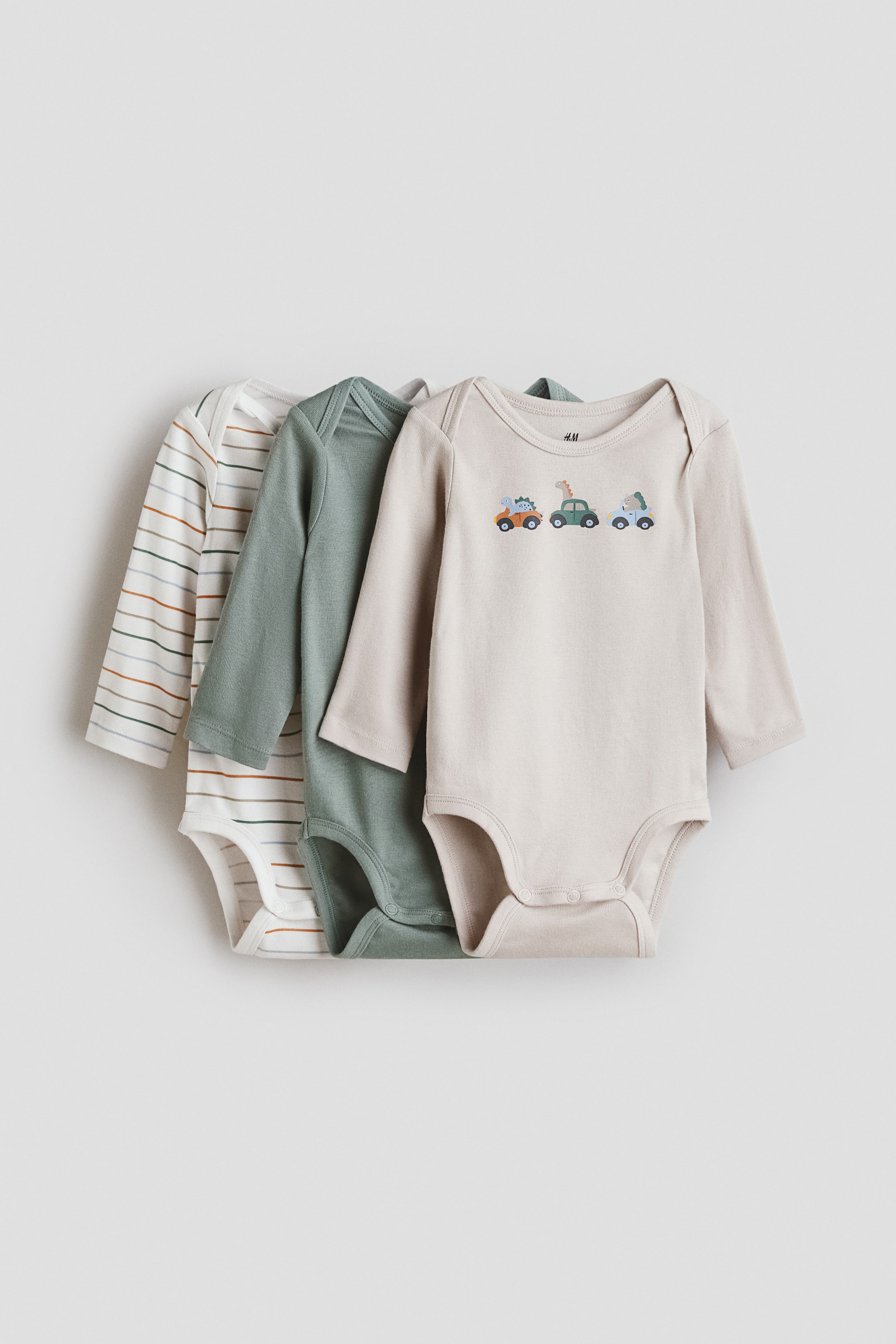View larger image: Long-sleeved bodysuits are arranged front-facing, featuring a light beige bodysuit with an embroidered cartoon vehicle design, a solid sage green bodysuit, and a white bodysuit with multicoloured horizontal stripes. All bodysuits feature an envelope neck and press-studs at the bottom.