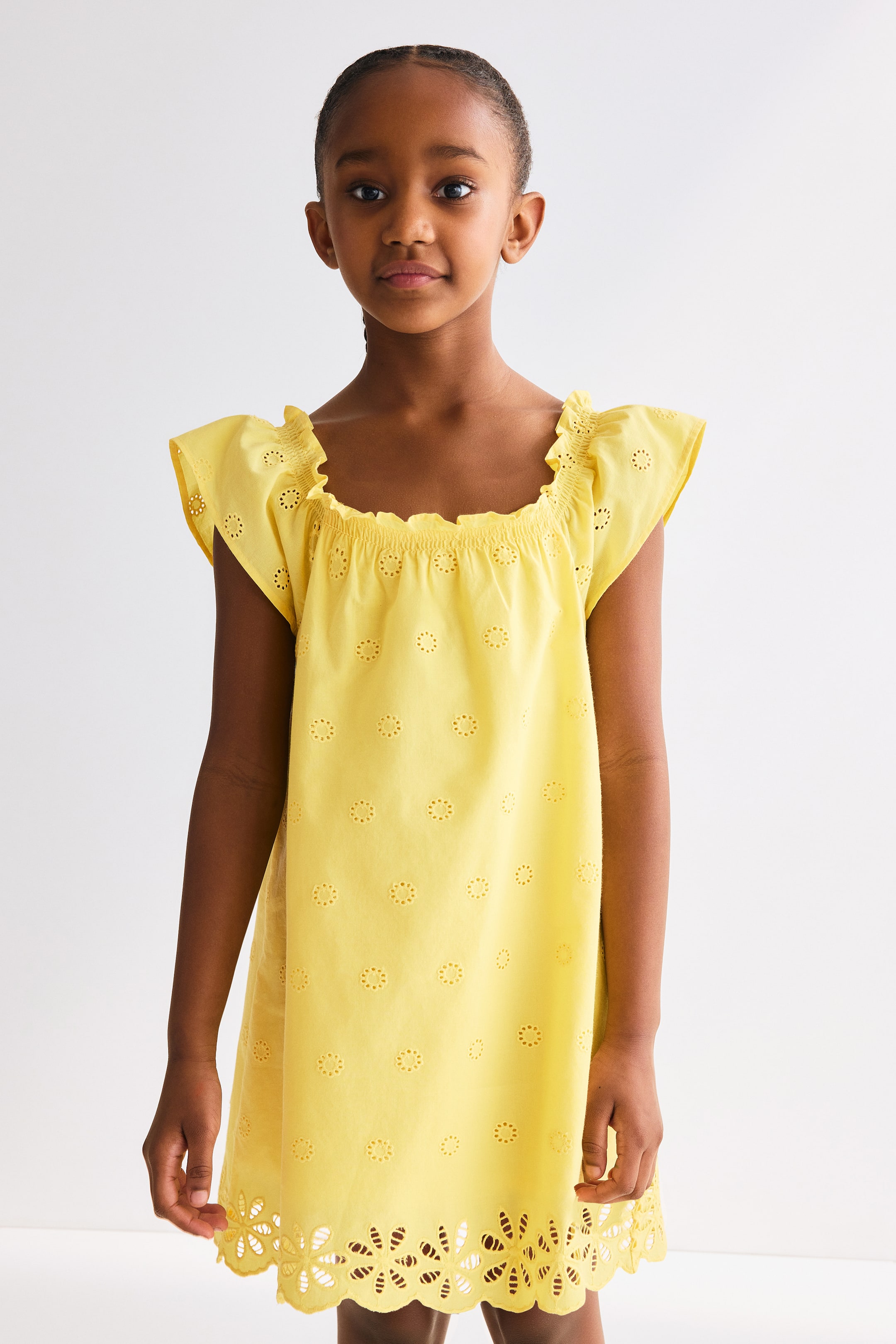 View larger image: The yellow dress boasts a square, elasticated neckline adorned with ruffles and short, ruffled cap sleeves. This dress highlights all-over eyelet embroidery, with a unique scalloped eyelet pattern embellishing the hem.