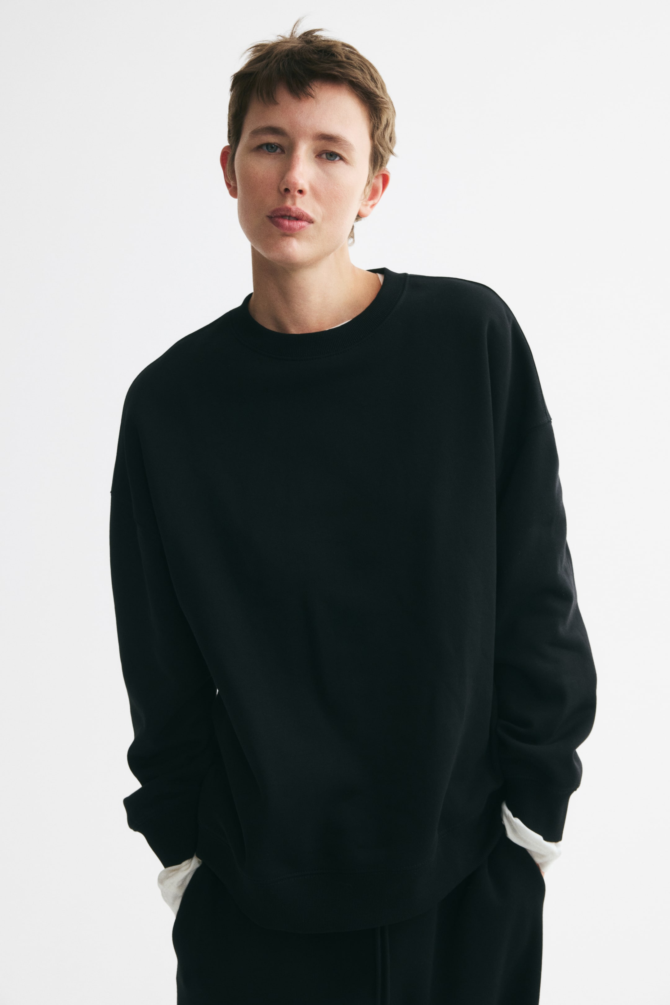 View larger image: The model is wearing an oversized black sweatshirt with a ribbed crew neckline, dropped shoulders, long sleeves, and ribbed cuffs and hem. A white undershirt is layered underneath, visible at the neckline and extending past the cuffs and hem.