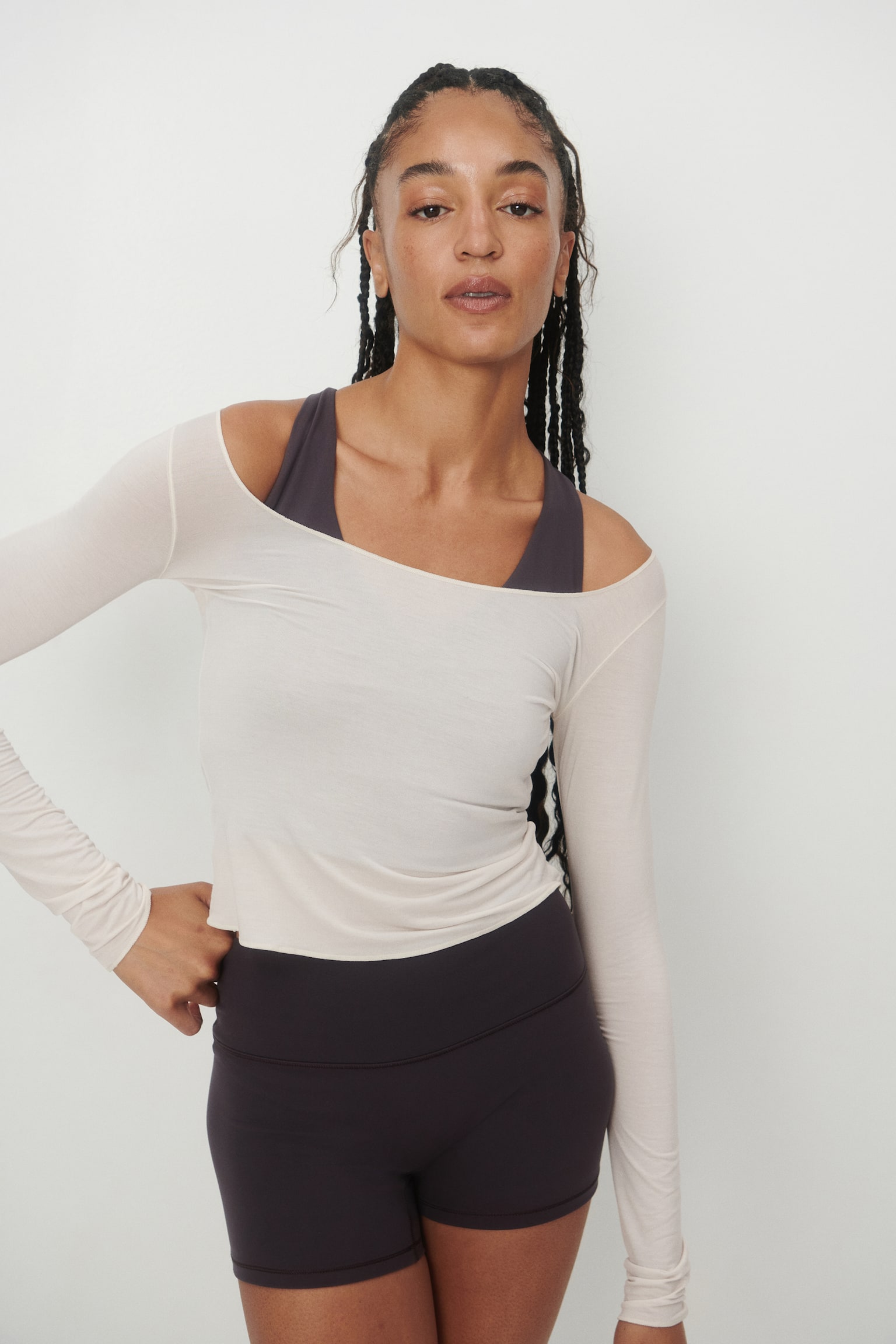A light cream long-sleeved top features a wide scoop neckline, long sleeves, and a cropped length with a raw-edge finish on the bottom hem and sleeve cuffs, all displayed from a front view. - 1