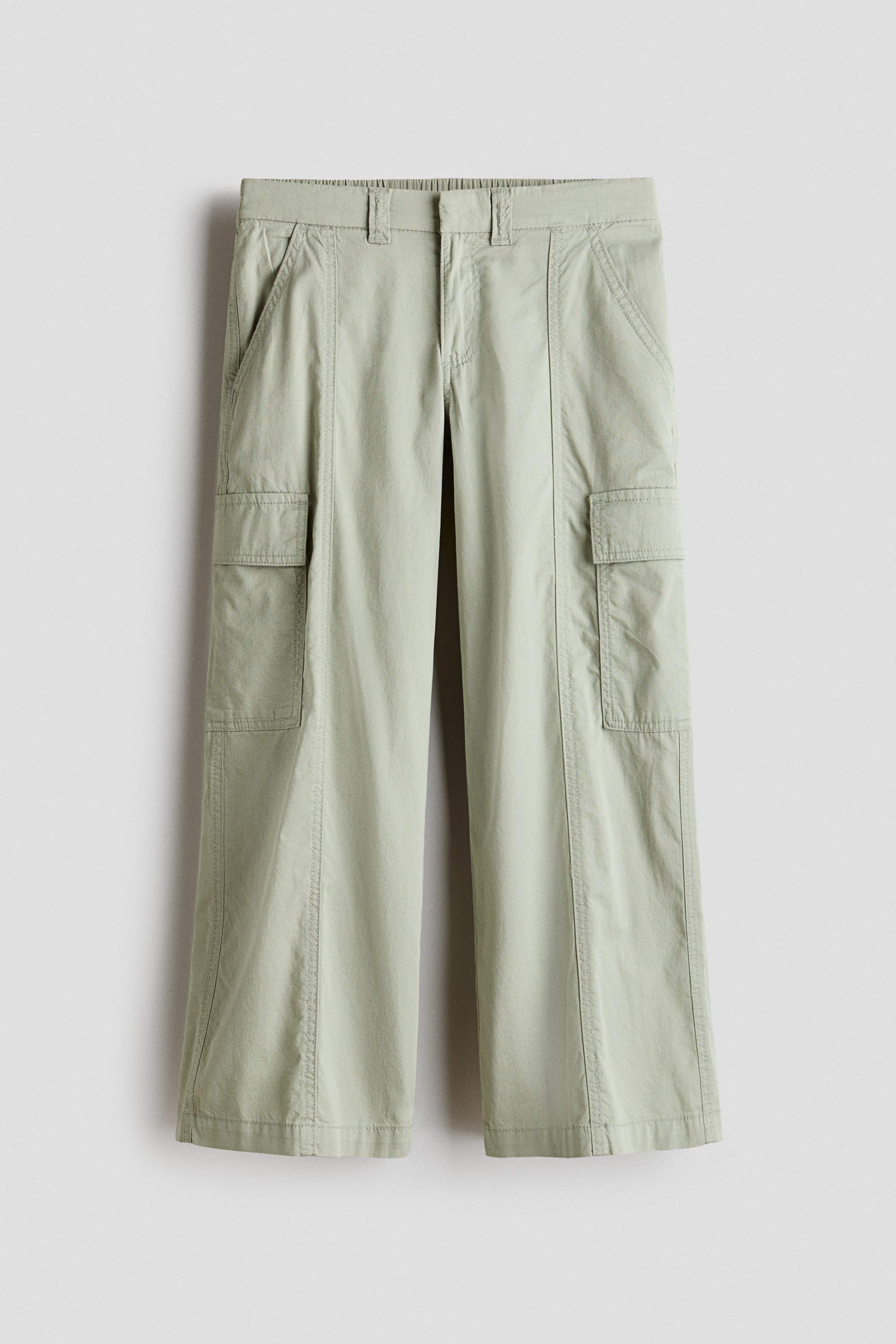 View larger image: Light green cargo pants are shown from the front, showcasing an elastic waistband with belt loops and side slash pockets. Large flap cargo pockets are visible on both thighs, and the wide legs display vertical seam details down the front.