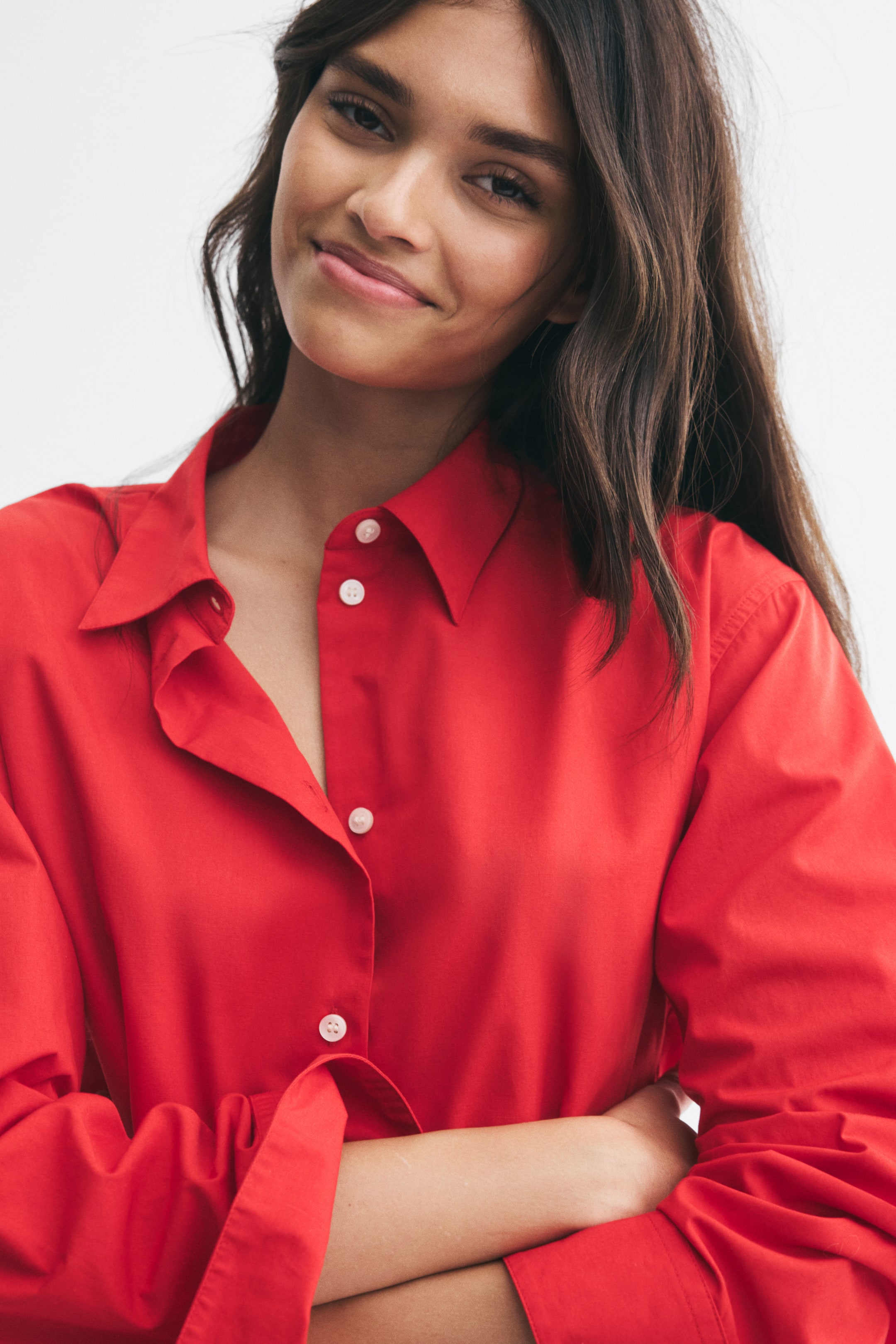 View larger image: A red cotton shirt featuring a collar and a white button-down front is worn by the model. The shirt has a relaxed fit with long sleeves and is shown with the collar open as the model poses with crossed arms.