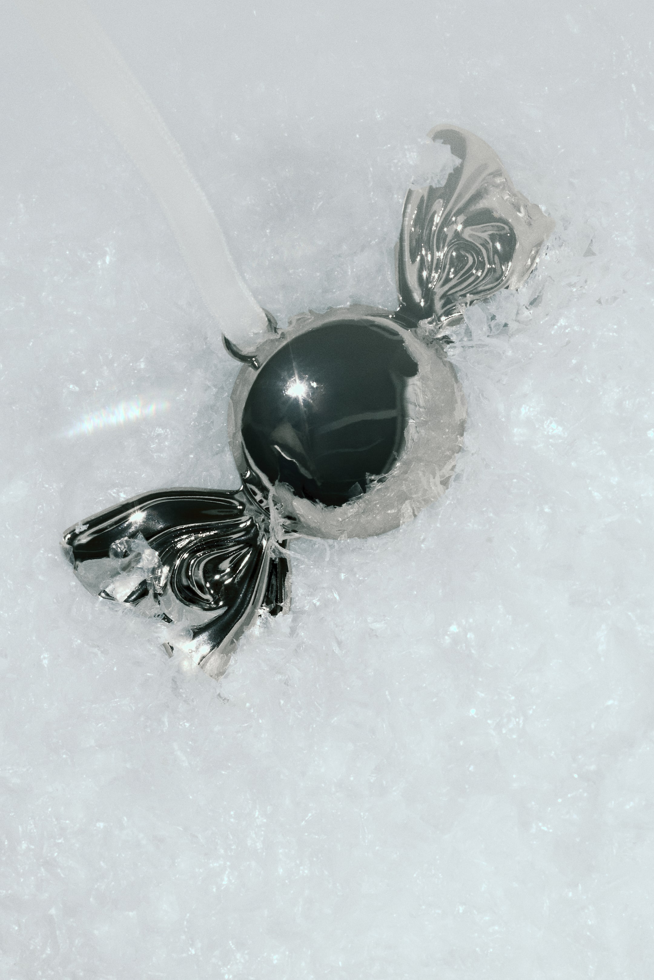 Grotere afbeelding bekijken: Een metalen kerstornament in de vorm van een wikkel snoepje met een hoogglanzende, gepolijste zilveren afwerking. Het ornament heeft een bolvormig middenstuk met uitlopende, gedraaide uiteinden en is bevestigd aan een dun wit ophanglint.