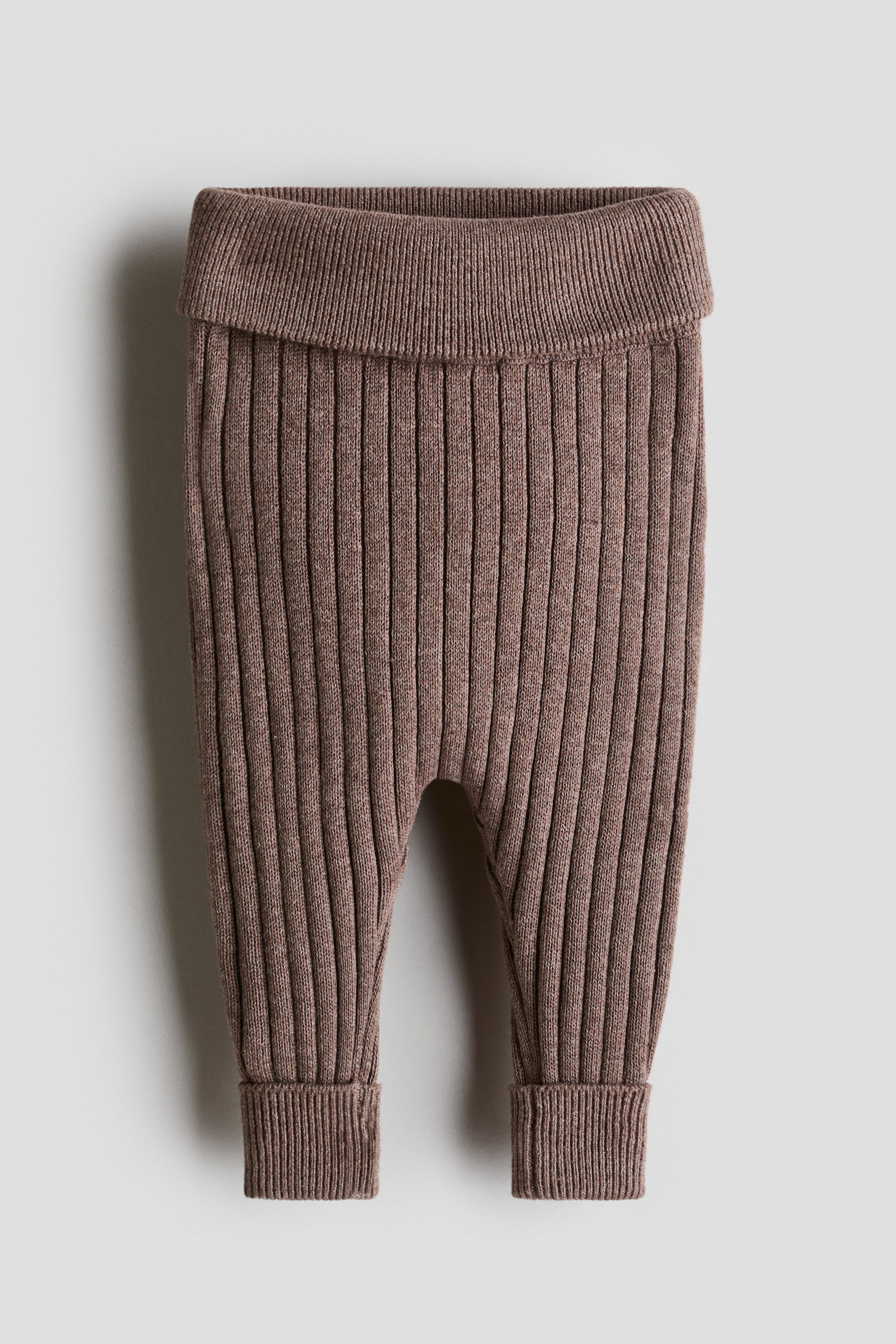 Grösseres Bild ansehen: Ein Paar braune Babyhosen aus Rippenstrick ist in einer frontalen Ansicht dargestellt und verfügt über einen breiten umklappbaren Bund sowie passende umgeschlagene Bündchen an den Knöcheln.
